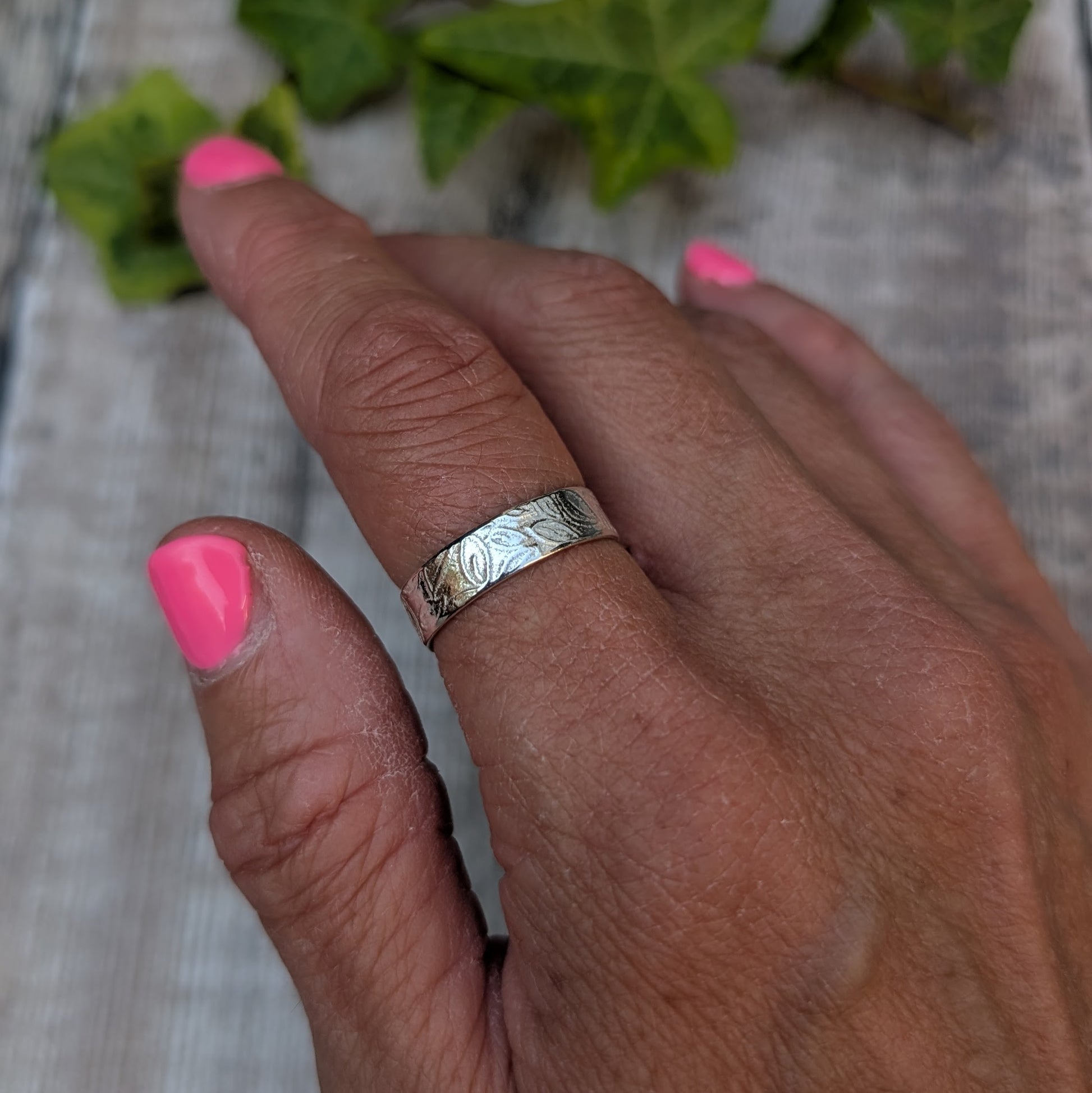 Silver 5mm Leaf Patterned Ring worn on a finger, showing the textured hand stamped leaf pattern around the silver band.