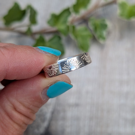 Silver 5mm Sunrise Ring handmade from recycled Sterling Silver with a hand stamped sunrise pattern, shown held between fingers.