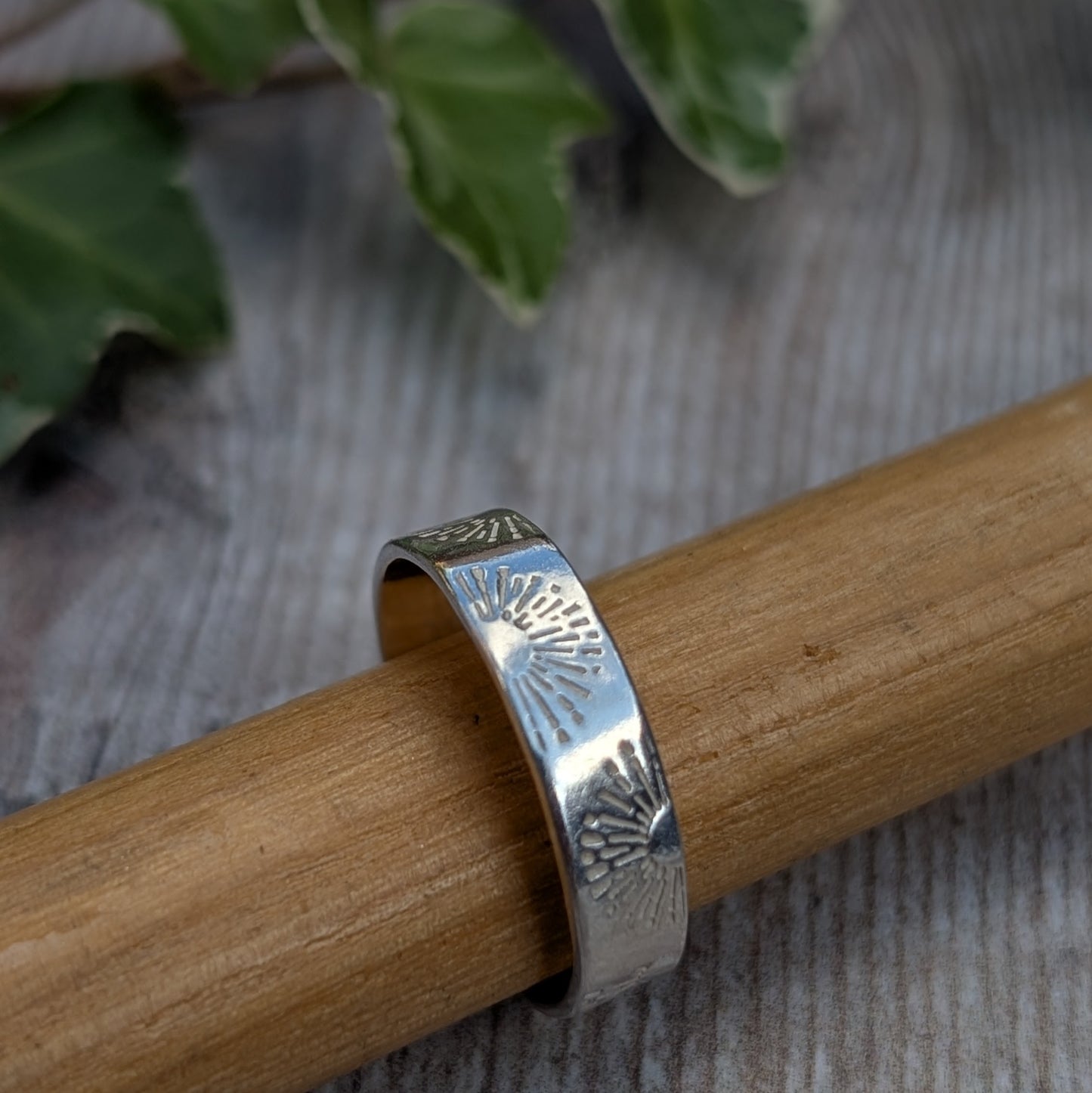 Close up of the Silver 5mm Sunrise Ring handmade from recycled Sterling Silver with a hand stamped sunrise pattern, displayed on a wooden ring mandrel.