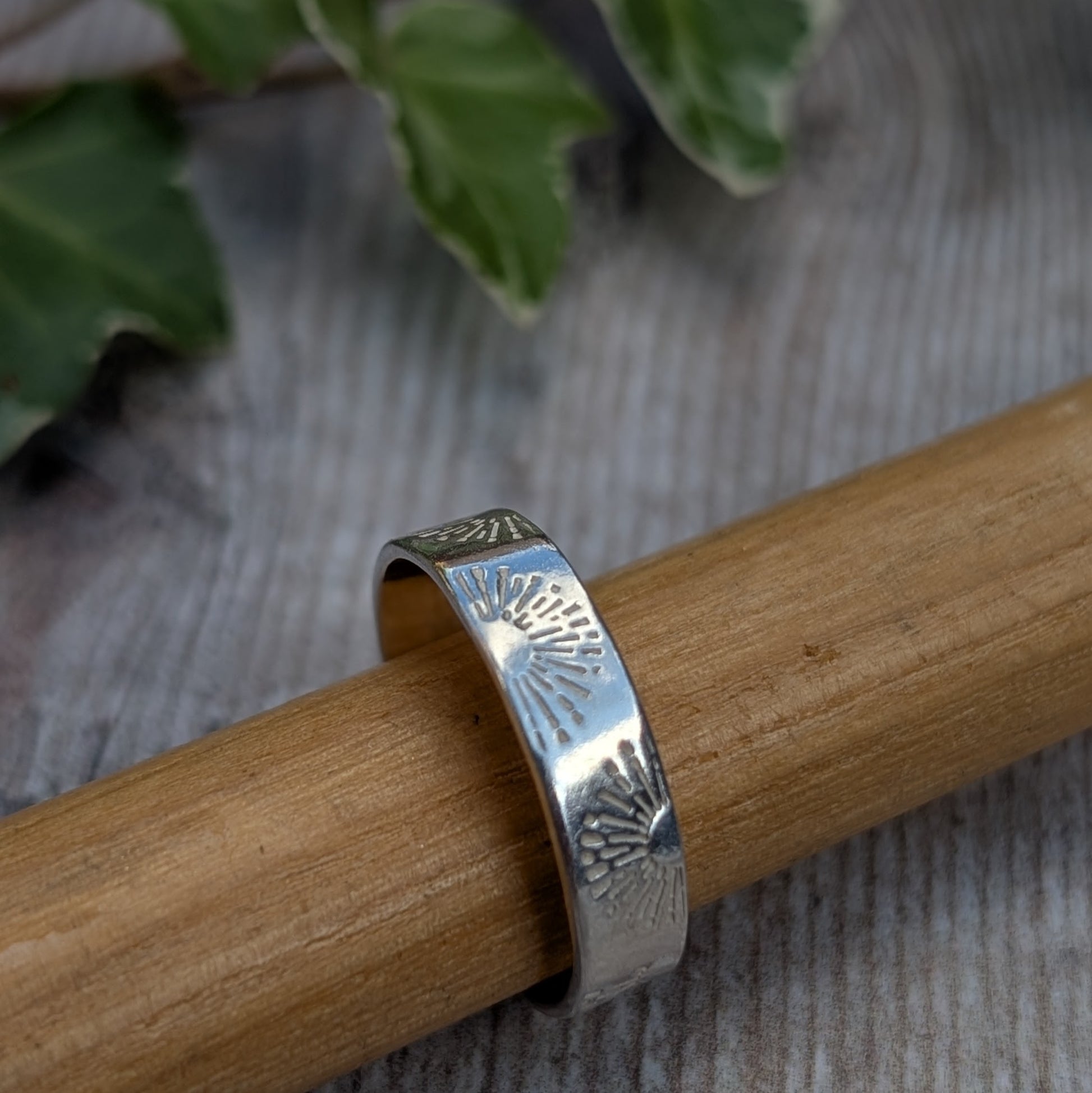 Close up of the Silver 5mm Sunrise Ring handmade from recycled Sterling Silver with a hand stamped sunrise pattern, displayed on a wooden ring mandrel.
