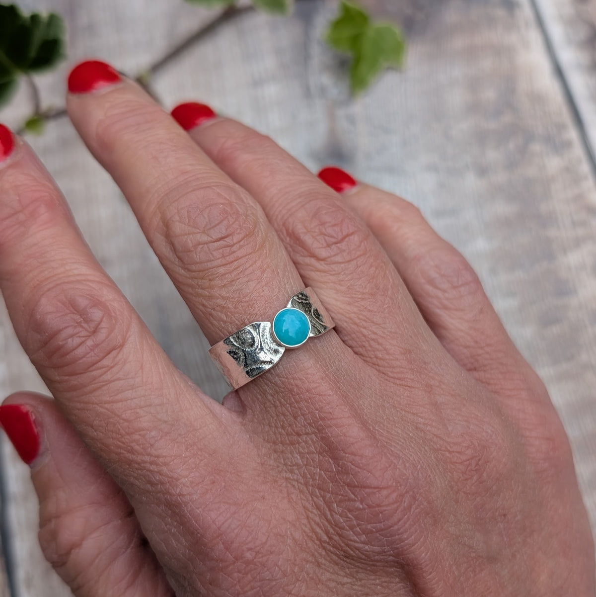 Silver oval patterned Amazonite wide band ring worn on a finger, showing the wide textured silver band and oval blue Amazonite stone from above.