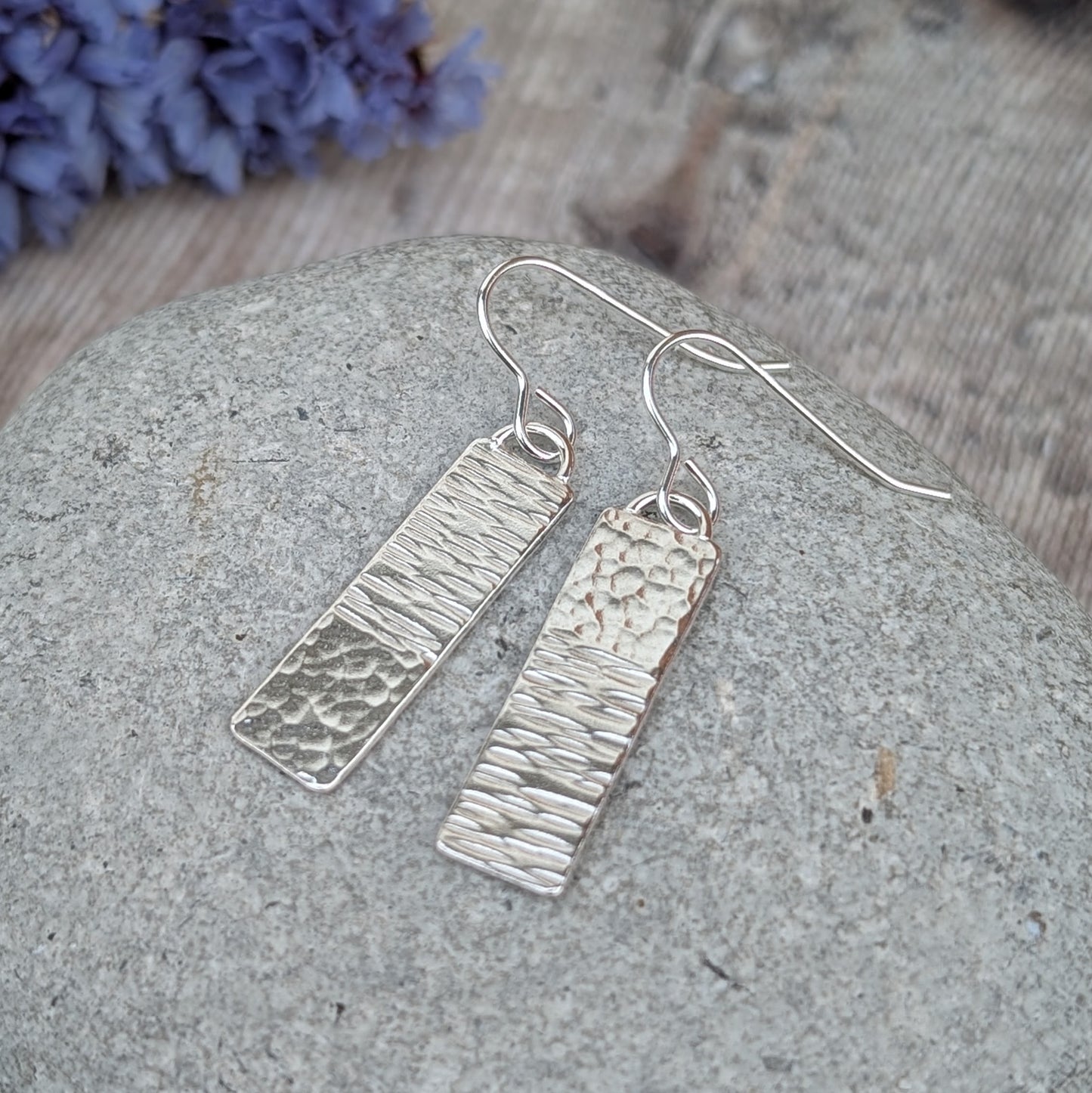 Silver asymmetrical hammered rectangle earrings displayed on a stone, showing the asymmetrical hammering on each rectangle
