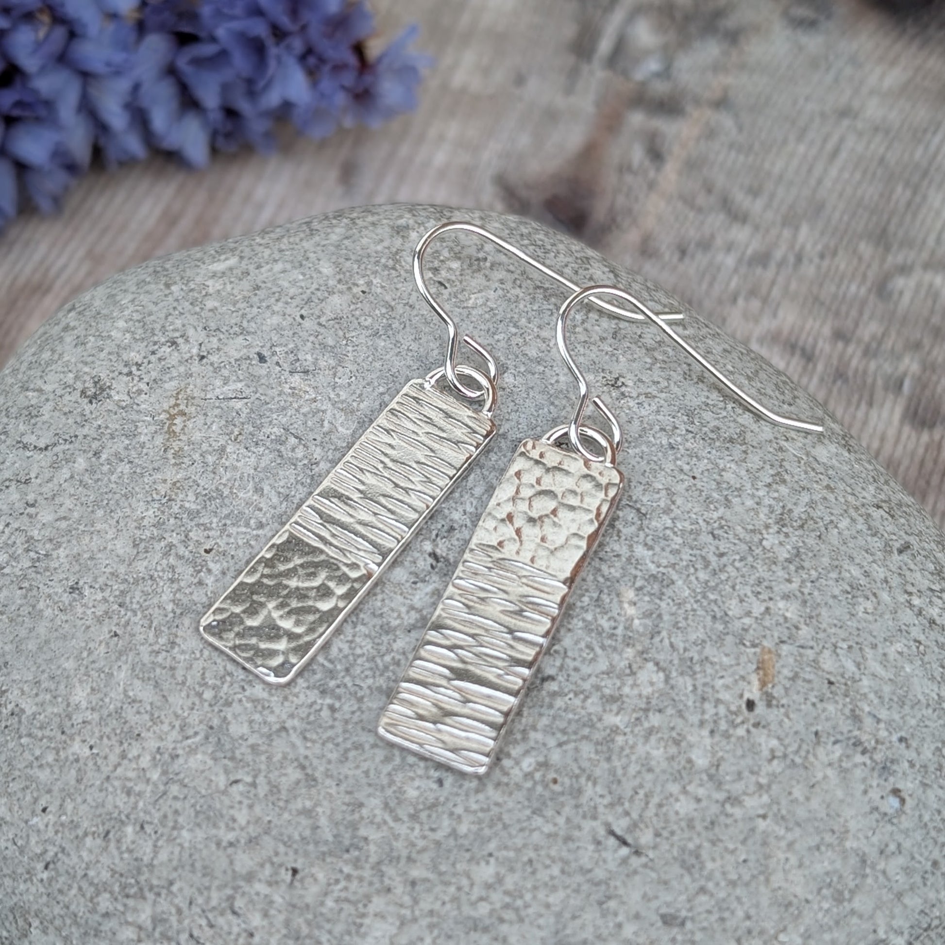 Silver asymmetrical hammered rectangle earrings displayed on a stone, showing the asymmetrical hammering on each rectangle