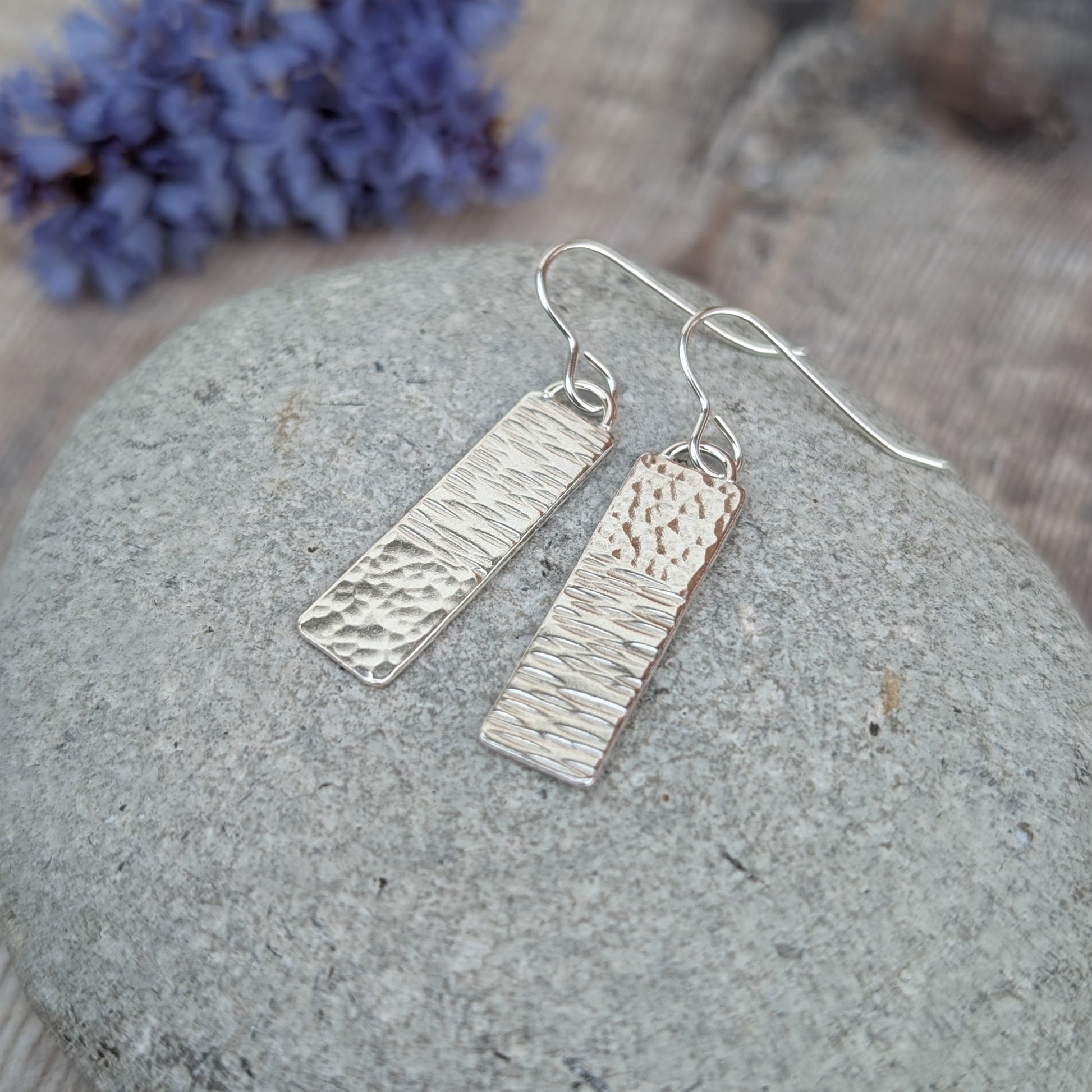 Silver asymmetrical hammered rectangle earrings with uneven hammered textures, photographed from above on a stone