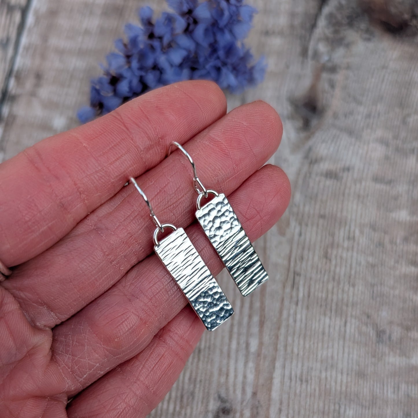 Silver asymmetrical hammered rectangle earrings held in the hand, showing size and texture detail