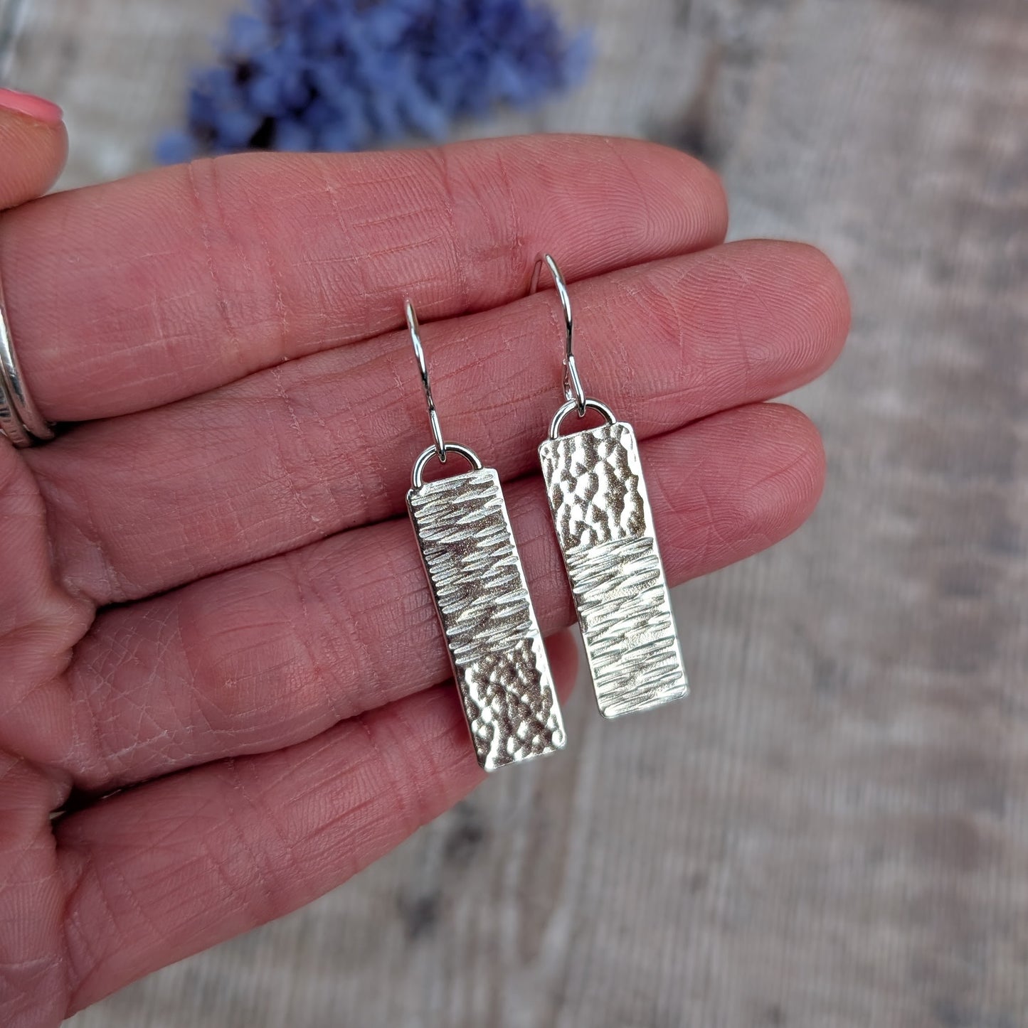 Silver asymmetrical hammered rectangle earrings resting on the hand, highlighting the different hammered finishes on each earring