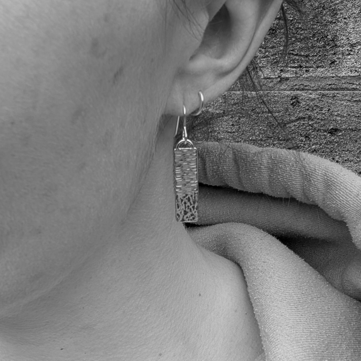 Silver asymmetrical hammered rectangle earring worn in the ear, showing drop length and fit