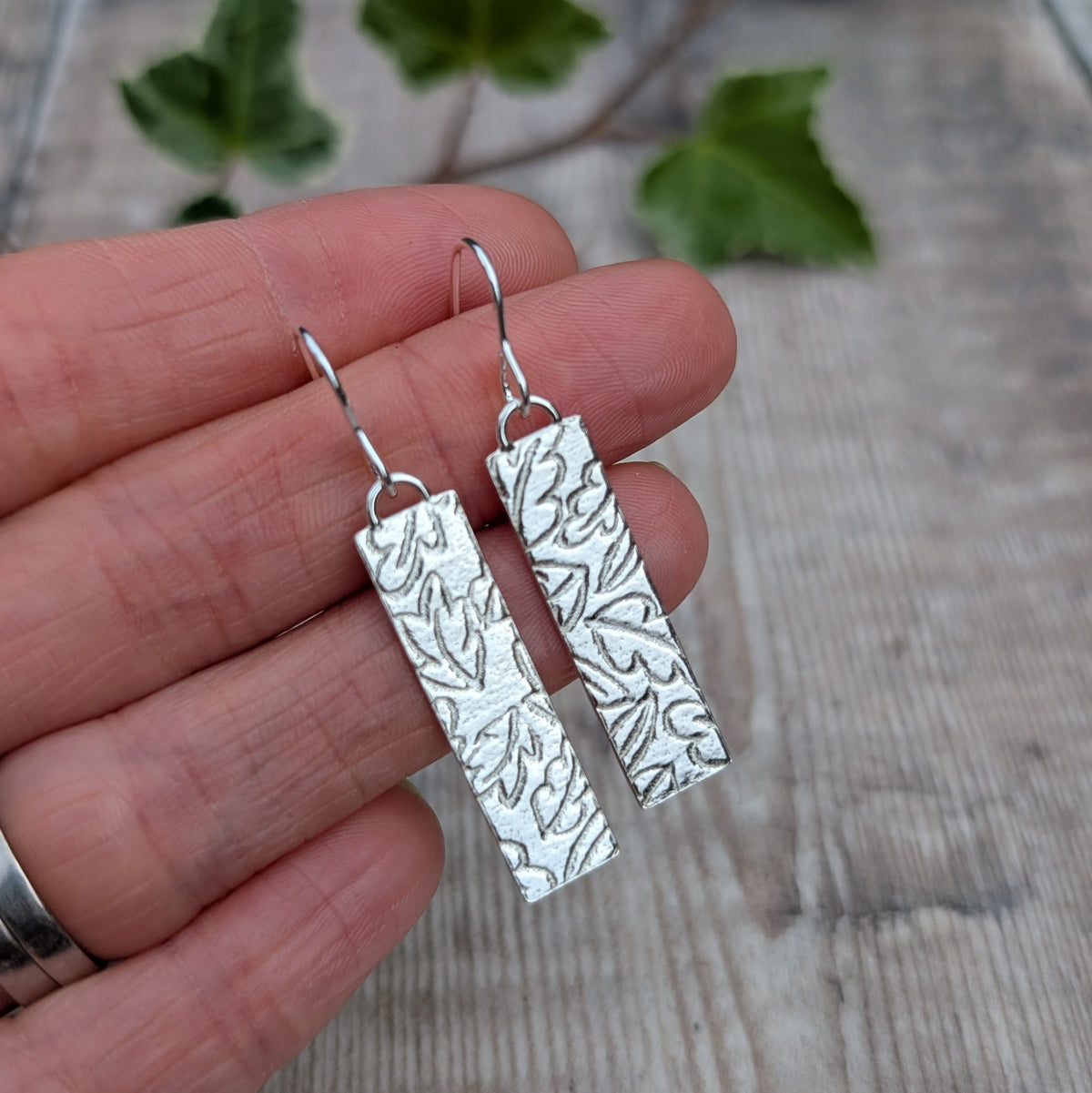 Silver autumn leaves long rectangle earrings handmade from recycled Sterling Silver, shown held in a hand to show their size and detailed leaf pattern.