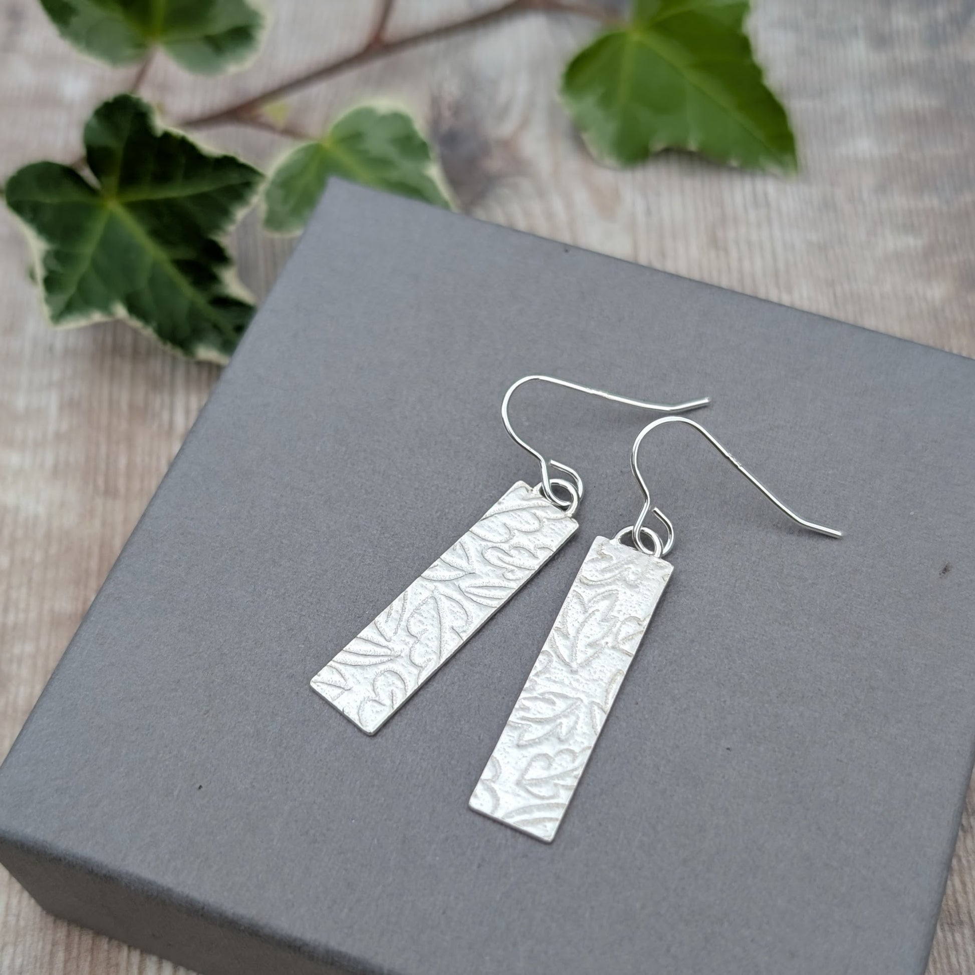 Silver autumn leaves long rectangle earrings handmade from recycled Sterling Silver, photographed at an angle on a grey jewellery box.