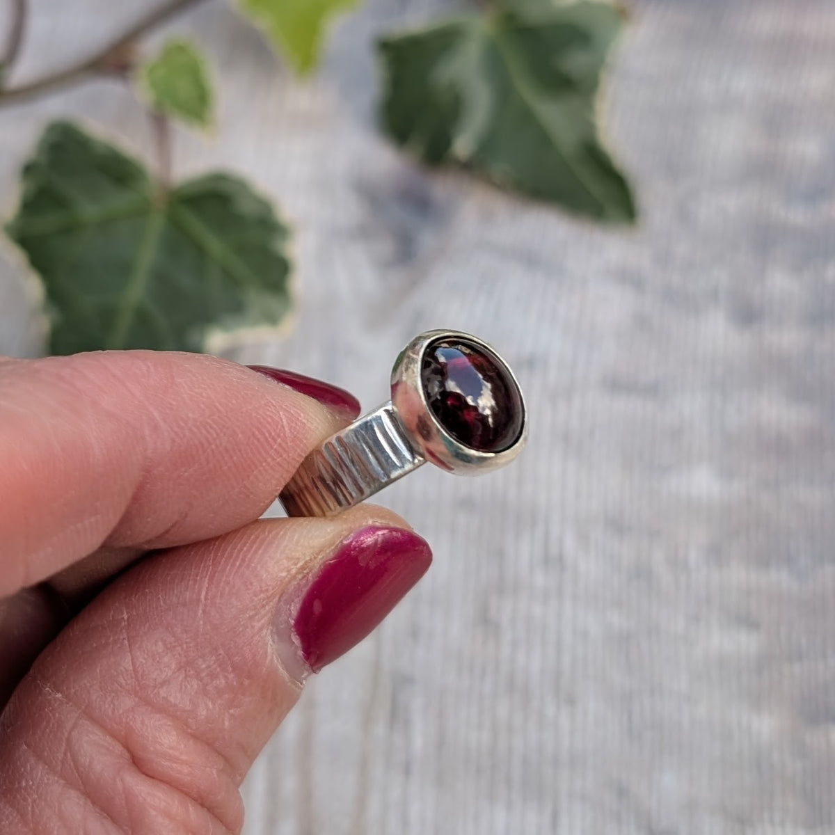 Close up side view of a silver bark textured garnet ring showing the hammered sterling silver band and deep red oval garnet gemstone.