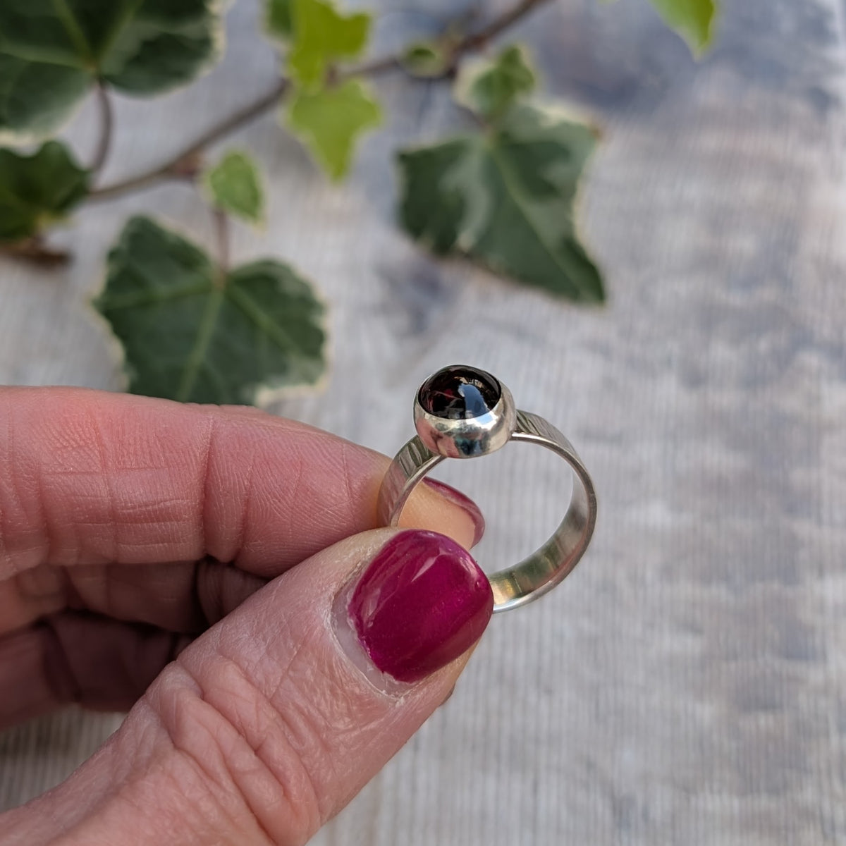 Side view of a handmade silver bark textured garnet ring held between fingers, showing the raised garnet setting and smooth inside of the silver band.