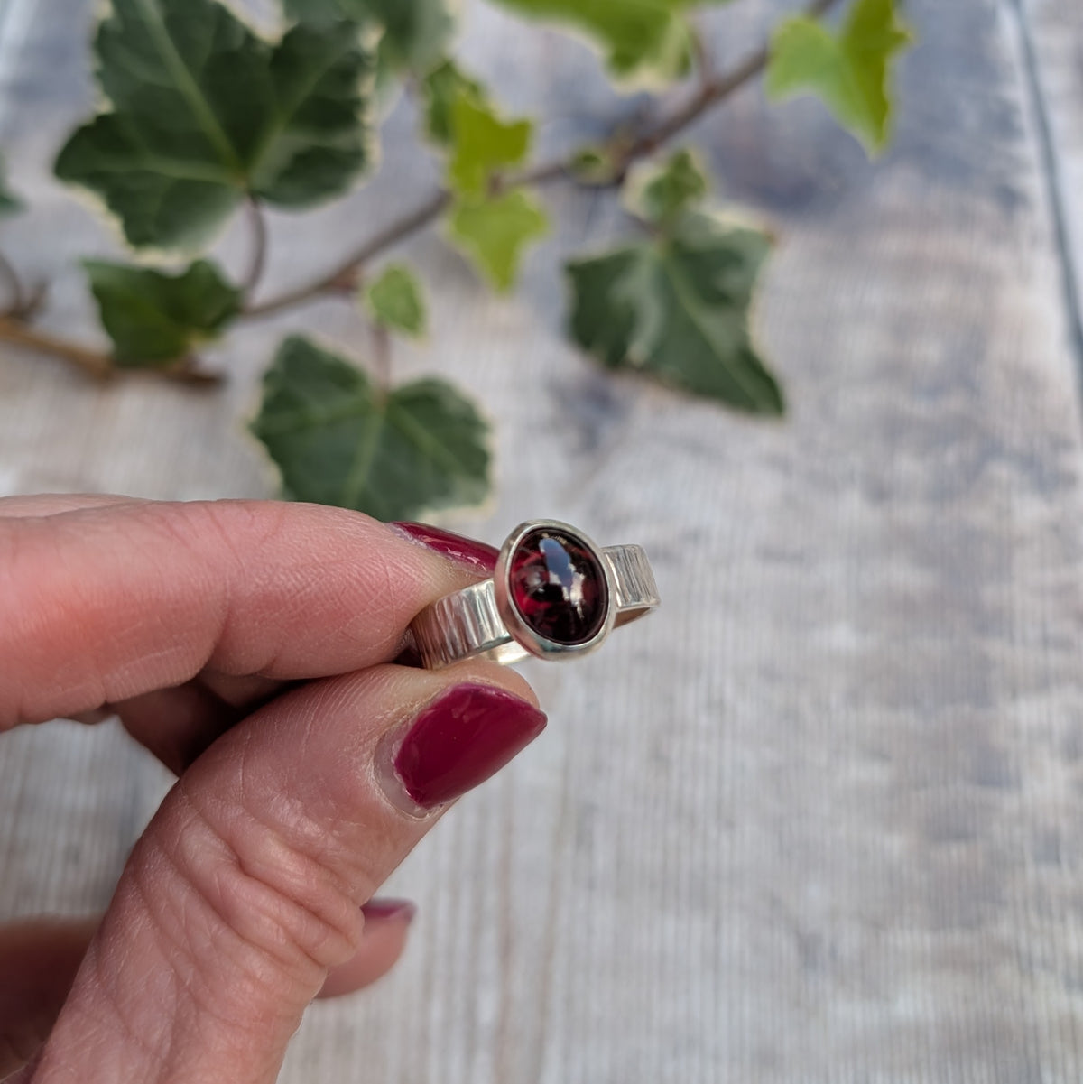 Front view of a silver bark textured garnet ring showing the deep red oval garnet stone and hand hammered bark pattern on the recycled sterling silver band.