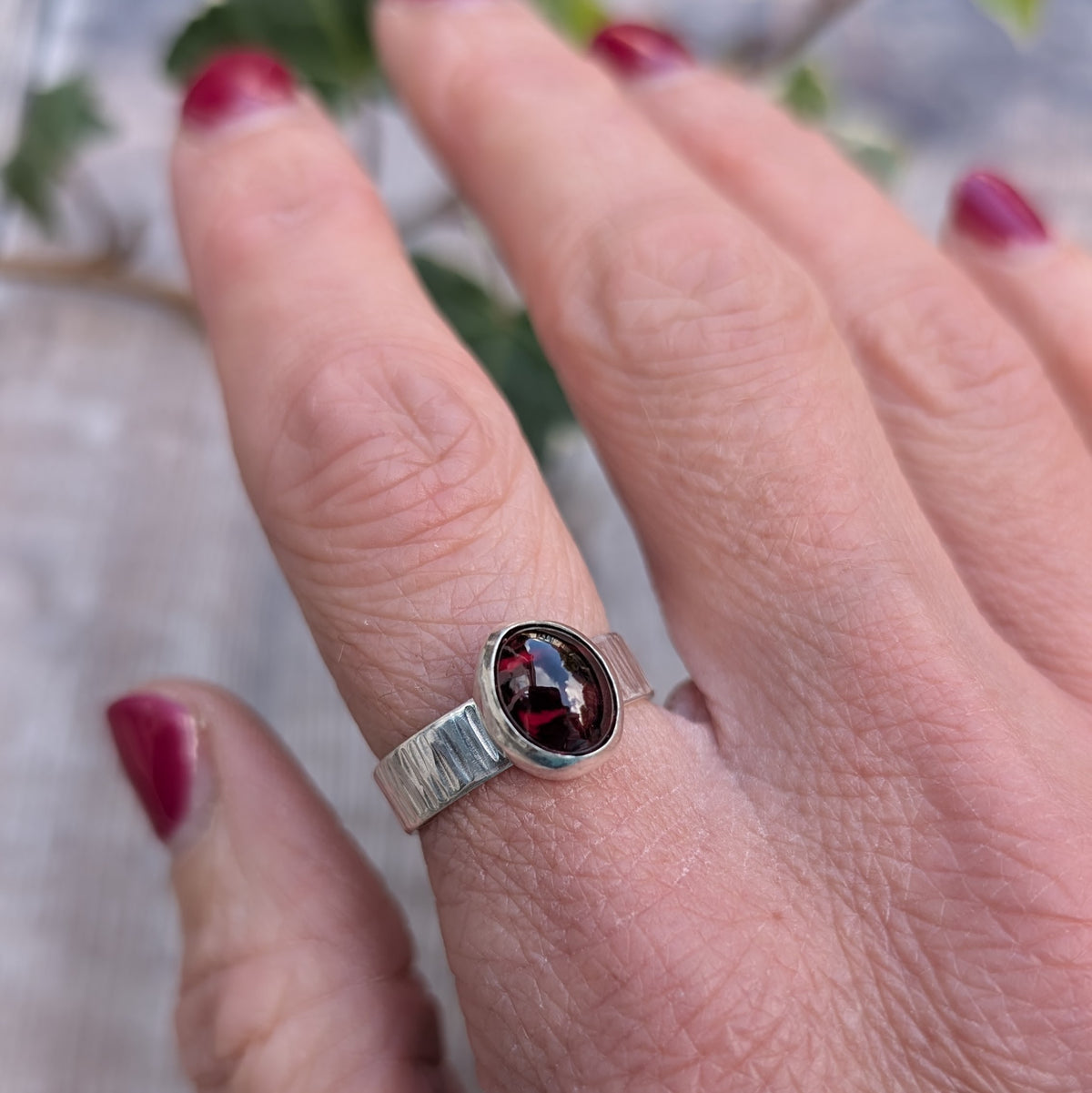 Close up of a silver bark textured garnet ring being worn, highlighting the deep red garnet gemstone and hand hammered texture on the wide silver band.