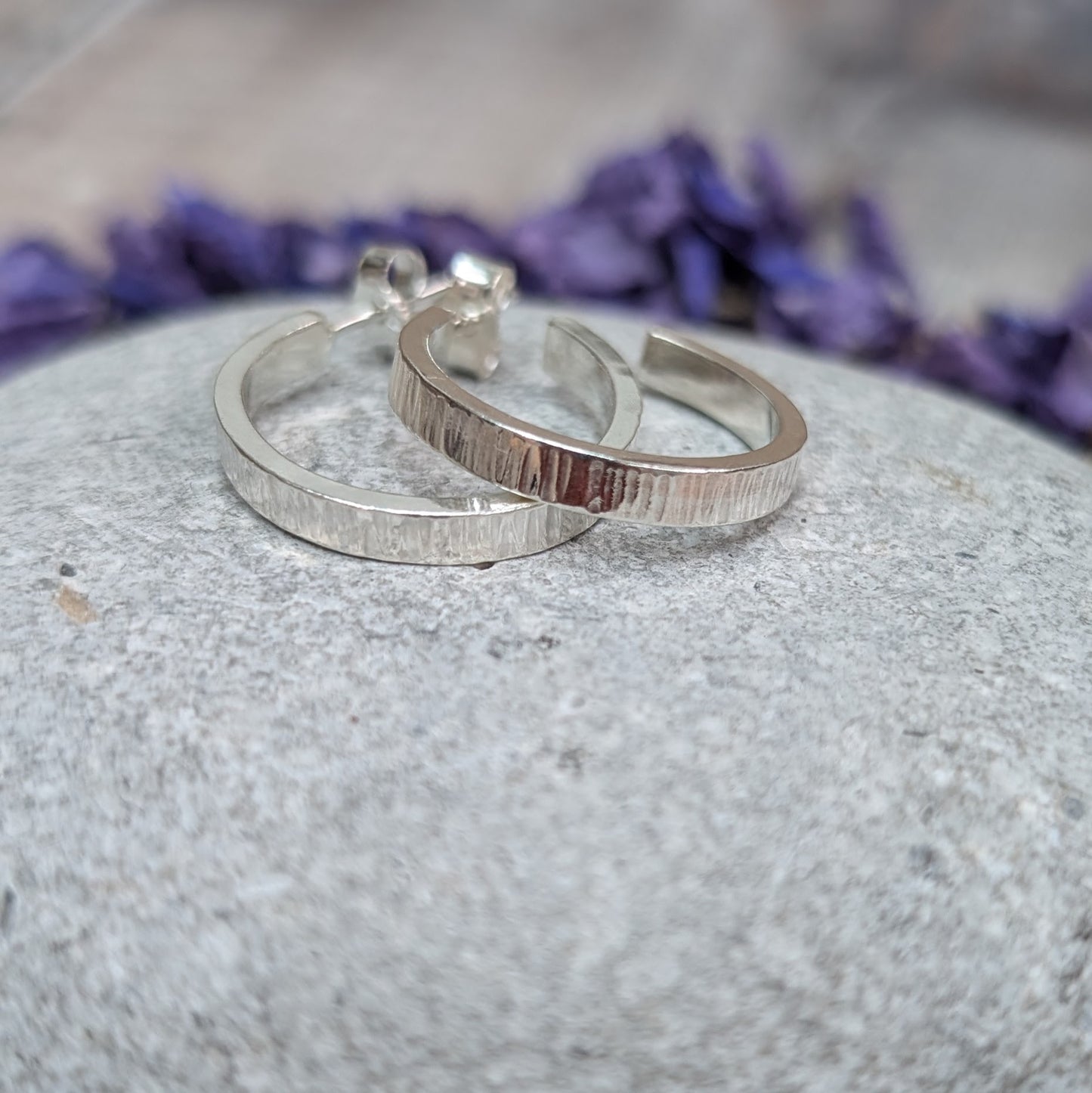 Close-up of Silver Bark Textured Hoop Earrings lying side by side on a grey stone, highlighting the fine bark-inspired texture.