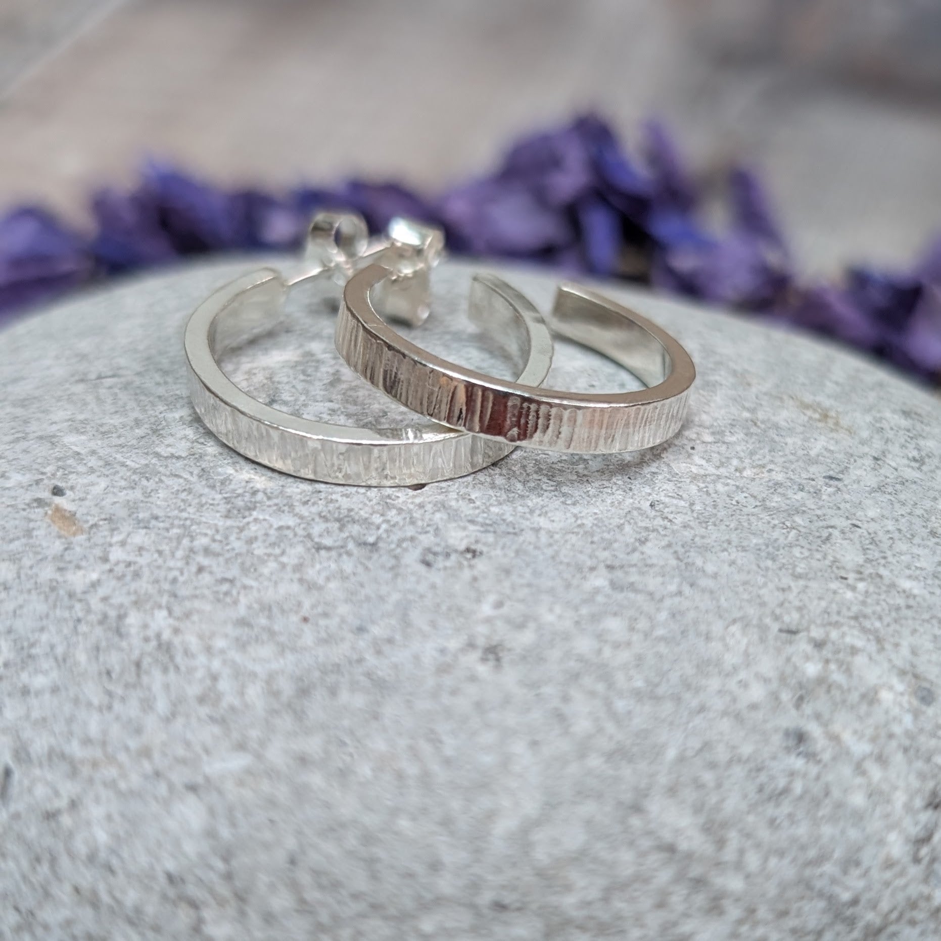 Close-up of Silver Bark Textured Hoop Earrings lying side by side on a grey stone, highlighting the fine bark-inspired texture.