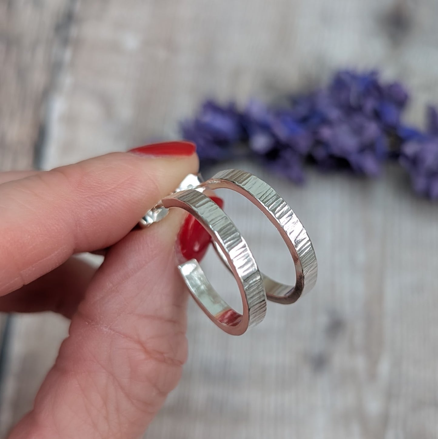 Hand holding Silver Bark Textured Hoop Earrings close up, showing the detailed linear bark texture and bright silver sheen.