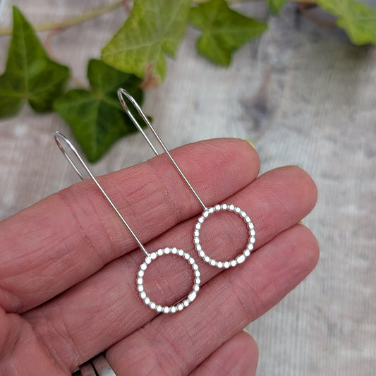 Close up of silver beaded circle long earrings resting on a hand, showing the recycled Sterling Silver beaded circle detail.