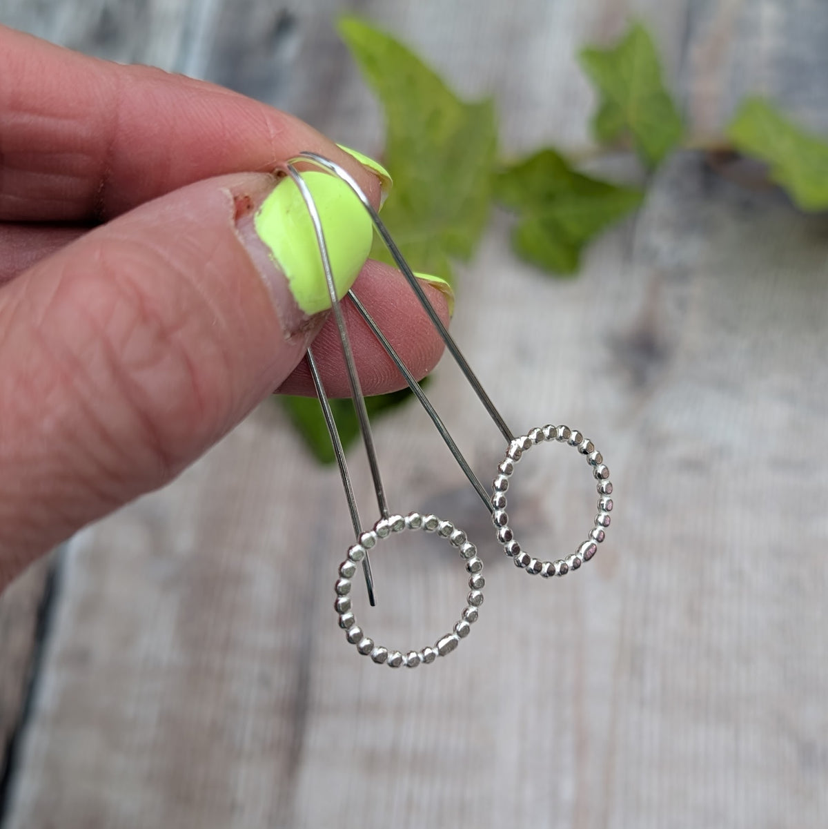 Close up of silver beaded circle long earrings held by hand, showing the open circle design and beaded silver texture.