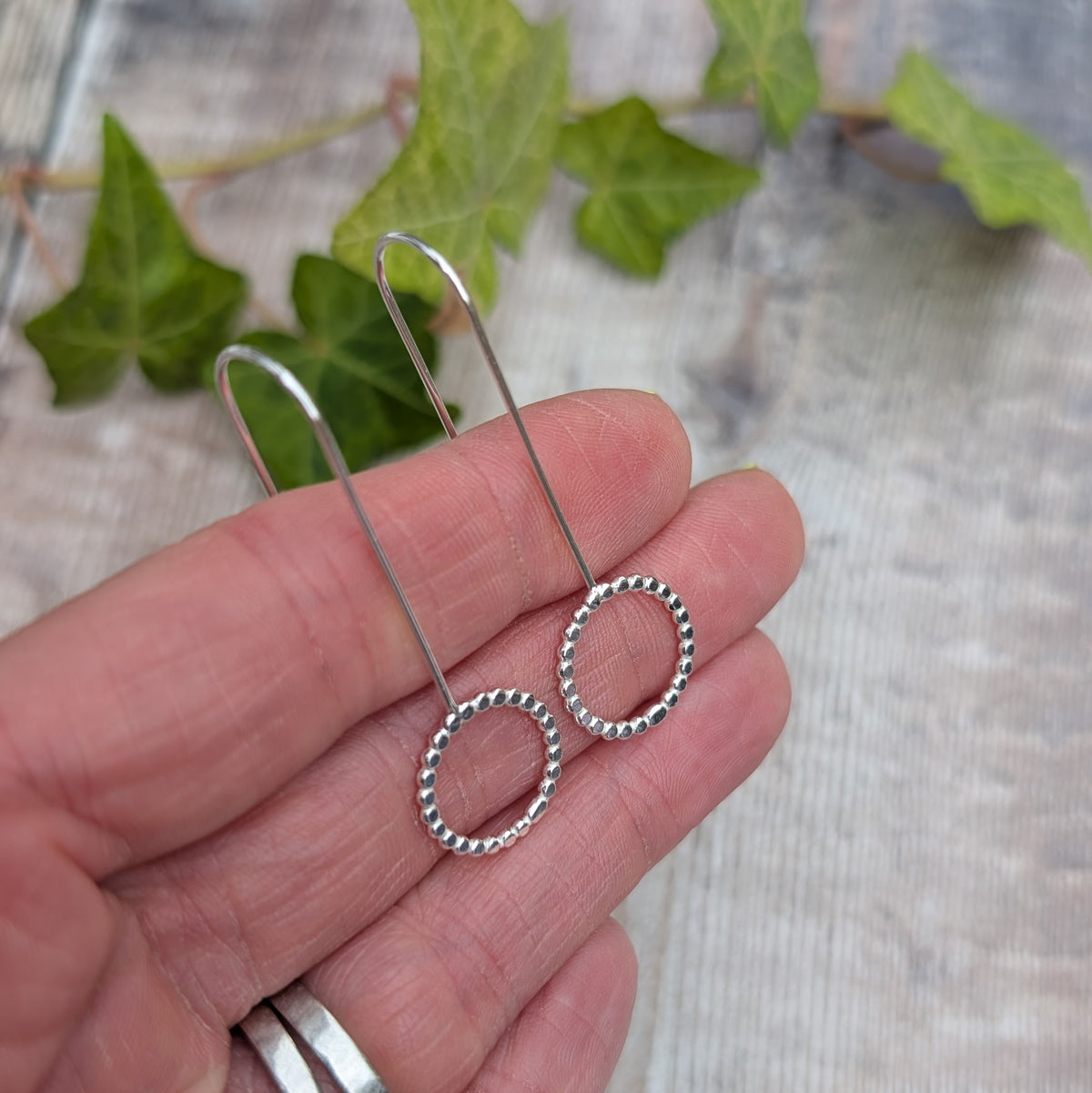 Silver beaded circle long earrings resting across a hand to show their size, shape and long ear wire design.