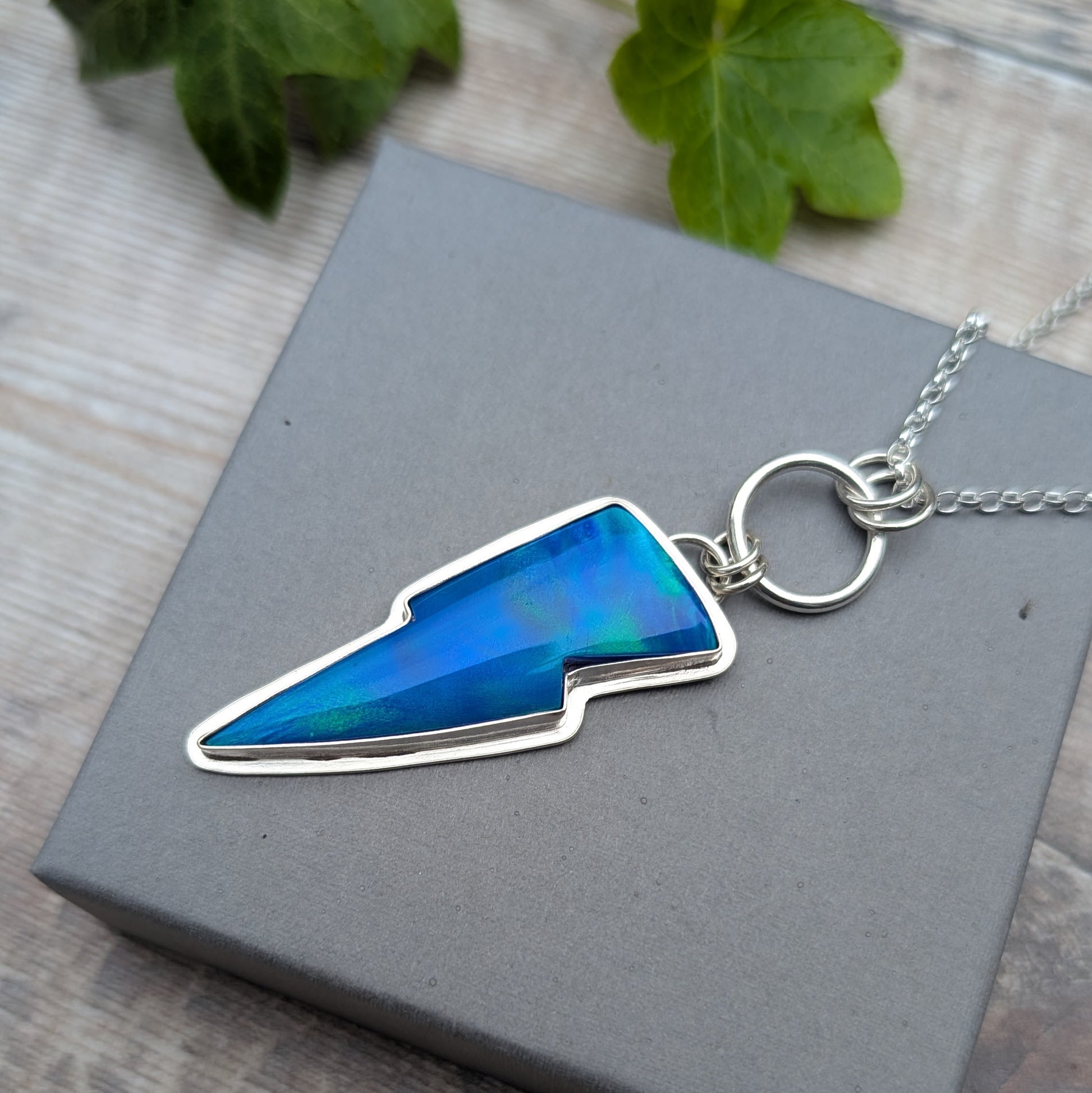 Close-up of the Silver Blue Aurora Opal Lightning Bolt Necklace on a grey jewellery box, featuring a vibrant blue Aurora Opal stone set in recycled sterling silver.