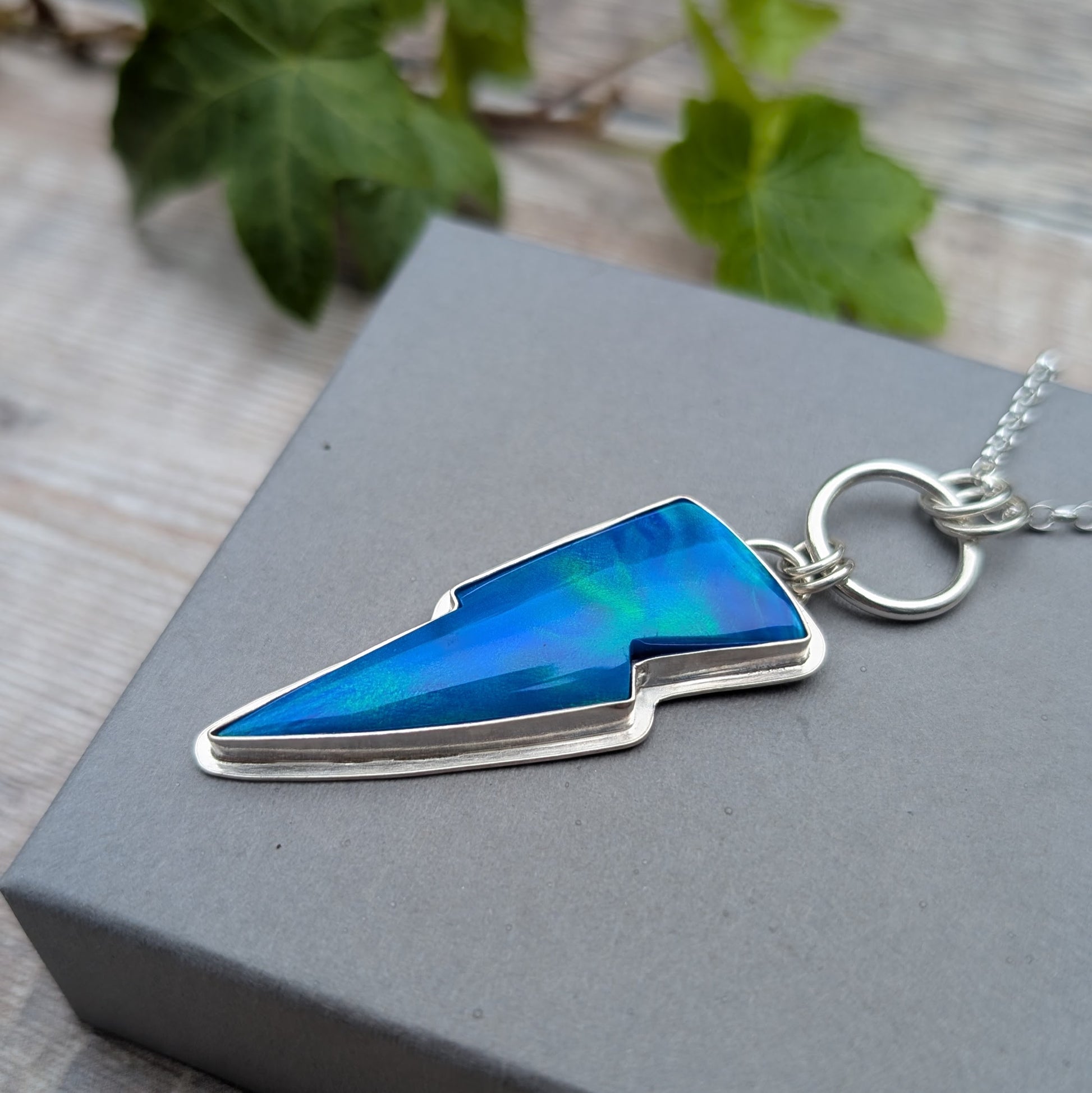 Silver Blue Aurora Opal Lightning Bolt Necklace handmade from recycled sterling silver, featuring a blue Aurora Opal stone in a hand made silver setting displayed on a grey jewellery box.