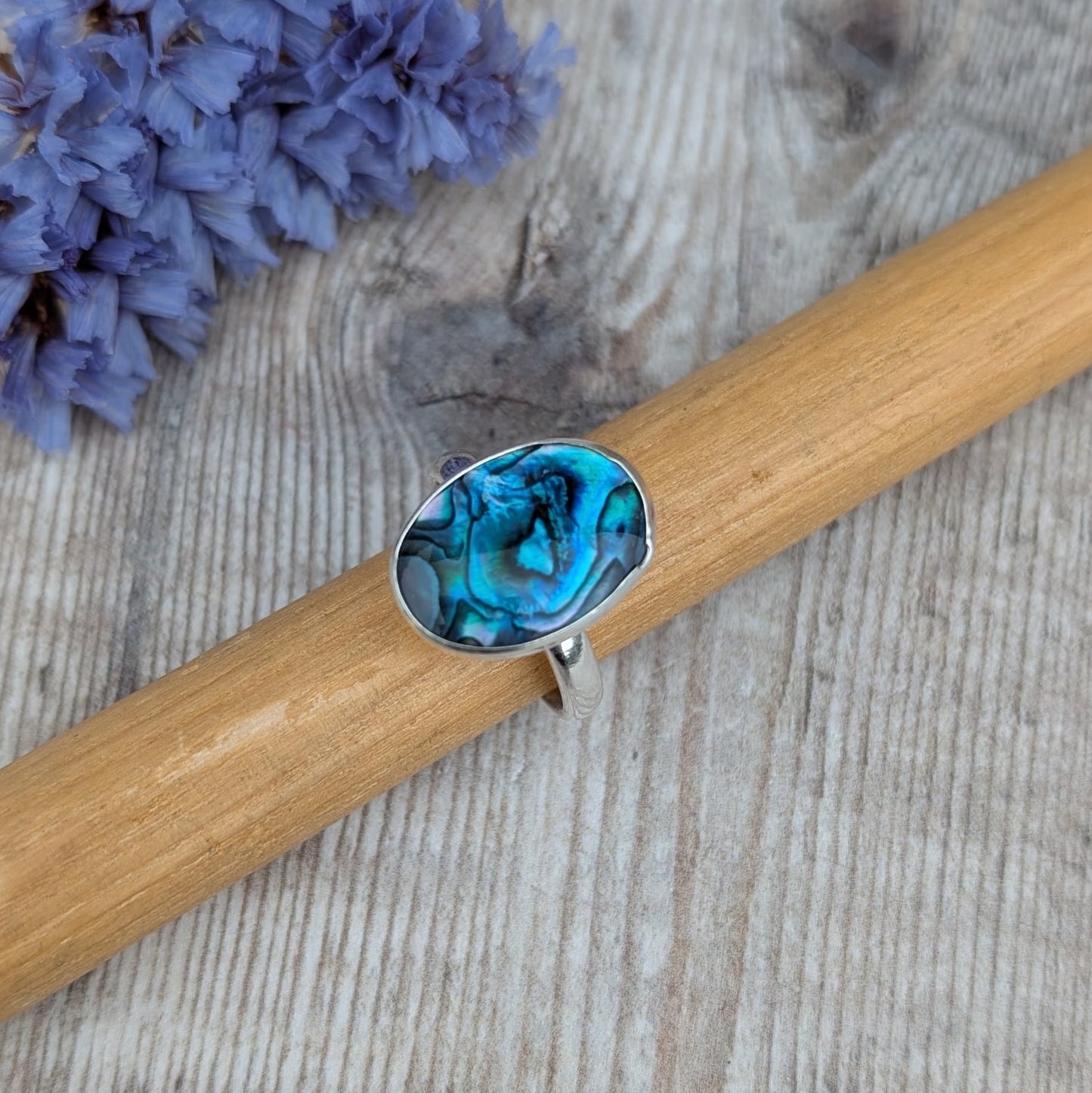 Silver Blue Paua Shell Ring resting on a wooden ring mandrel showing the oval blue Paua Shell set in recycled Sterling Silver.