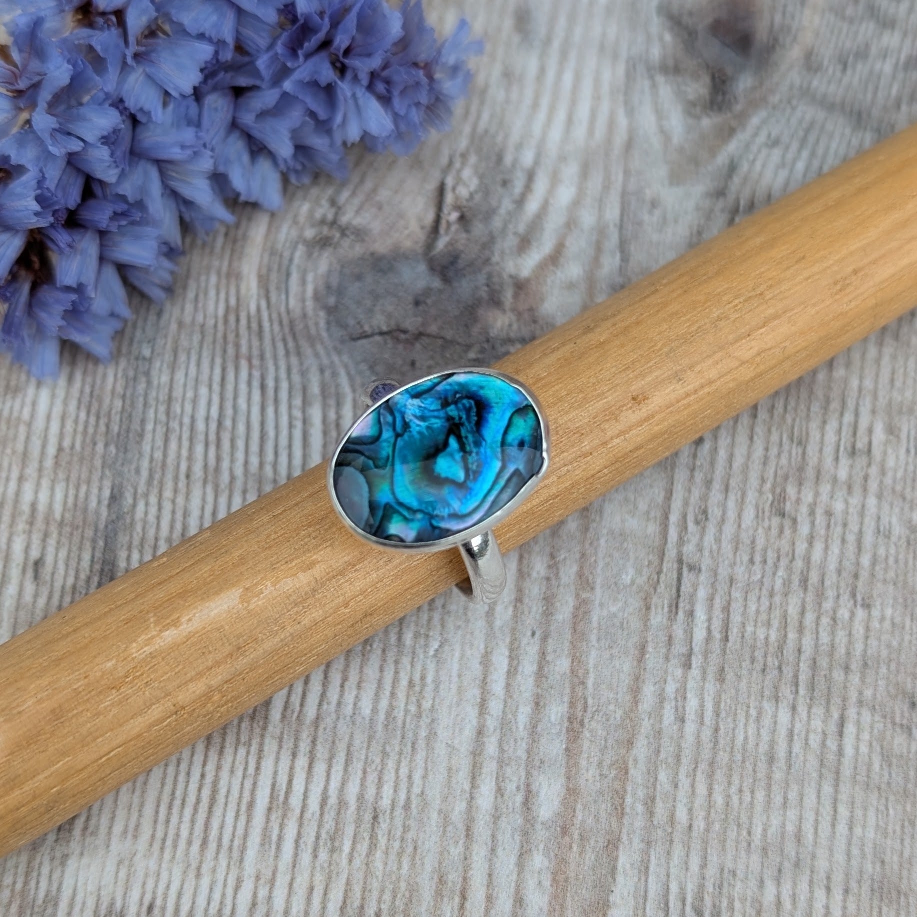 Silver Blue Paua Shell Ring resting on a wooden ring mandrel showing the oval blue Paua Shell set in recycled Sterling Silver.