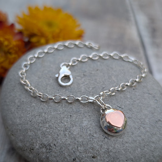 Silver Bracelet with Silver Pebble and Copper Heart Charm shown flat on a stone, focusing on the rounded pebble shape and copper heart detail.
