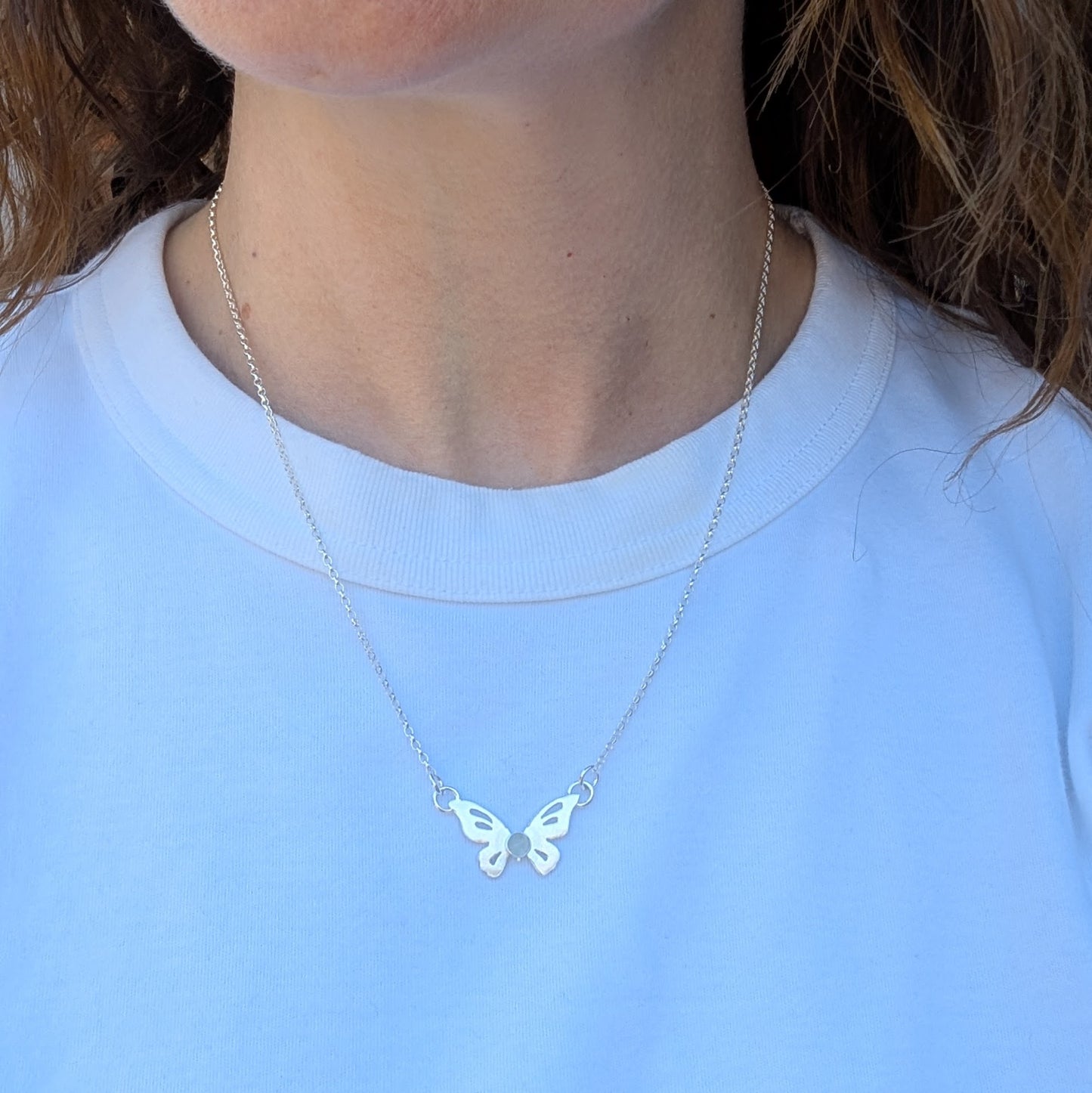 Silver Butterfly Necklace with Aquamarine worn on a person with a simple top, showing how it sits on the neckline