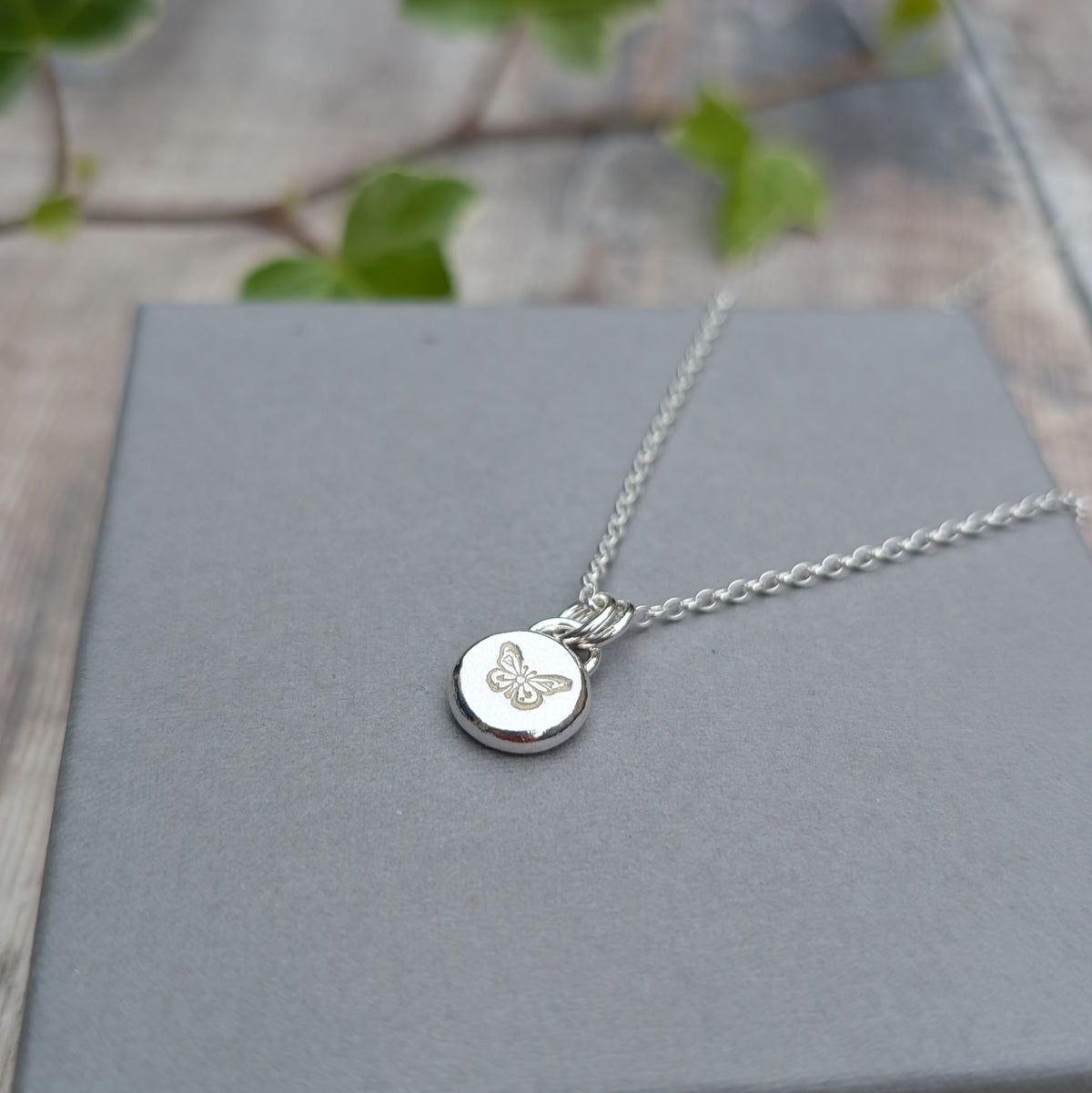 Silver butterfly pebble necklace handmade from recycled Sterling Silver, with a stamped butterfly design on a small round silver pendant.