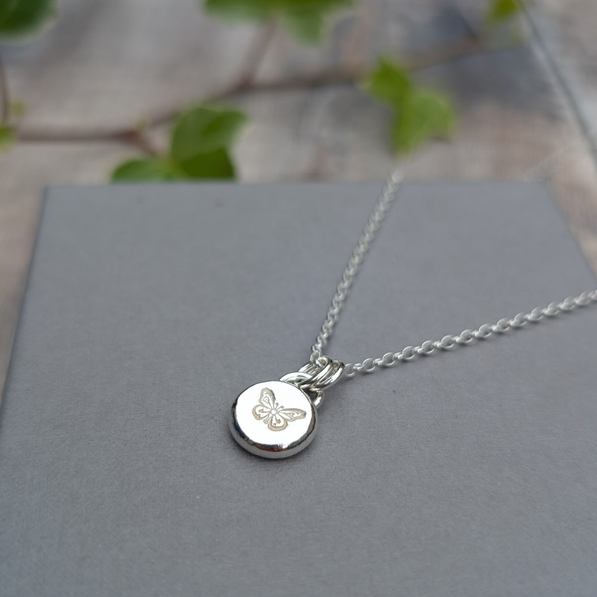 Close up of a silver butterfly pebble necklace showing the hand stamped butterfly detail on the recycled Sterling Silver pendant.