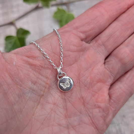 Silver butterfly pebble necklace held in a hand, showing the size and hand stamped butterfly design on the small silver pendant.