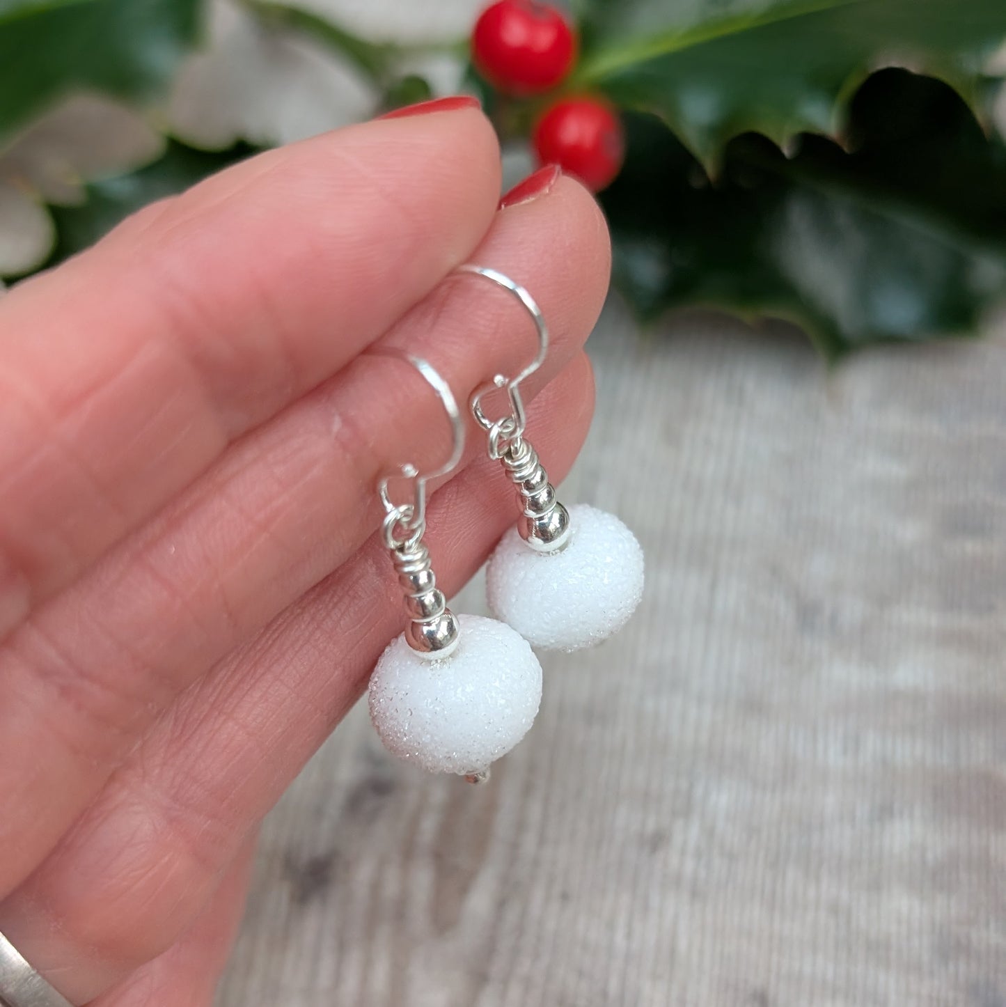 Close-up of a hand holding a pair of Silver Christmas Snowball Lampwork Glass Earrings, showing the frosted white glass beads with a soft, snow-like texture and sterling silver details.