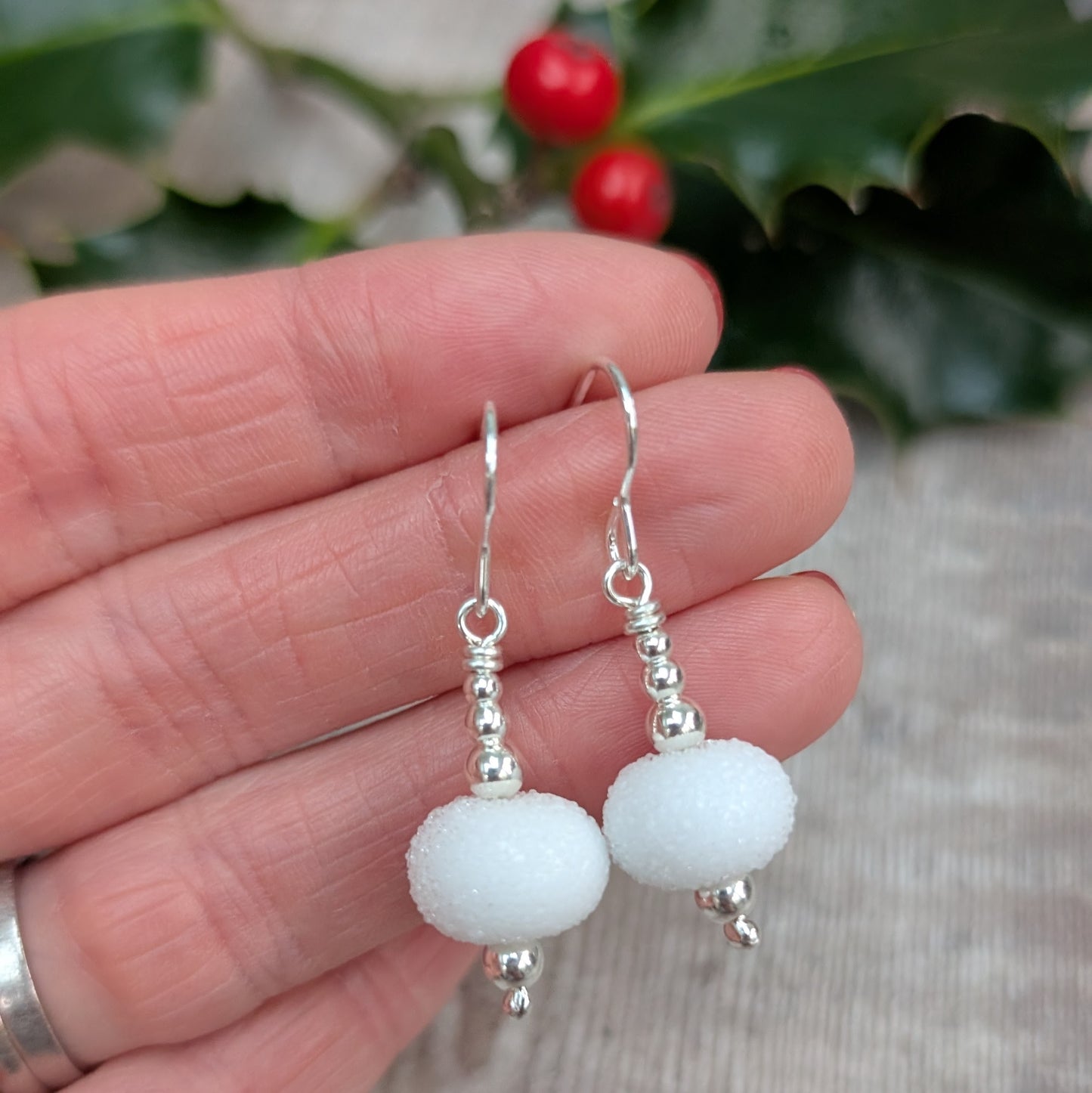 Close-up of the Silver Christmas Snowball Lampwork Glass Earrings held between fingers, highlighting the textured white glass beads and polished silver accents.