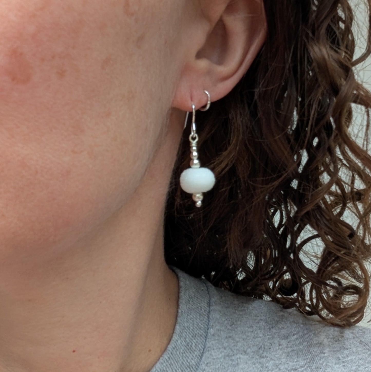 A person wearing one of the Silver Christmas Snowball Lampwork Glass Earrings, showing how the frosted white bead hangs from the sterling silver hook.