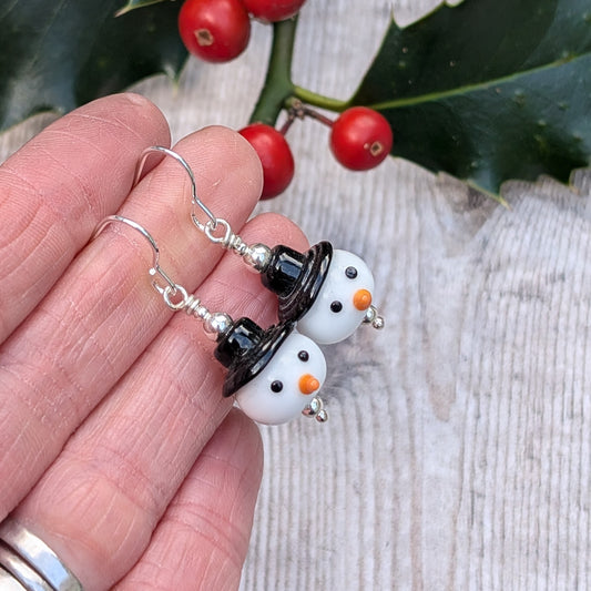 Close-up of the Silver Christmas Snowman Lampwork Glass Earrings held between fingers, highlighting the detailed glass snowman faces and polished silver fittings.