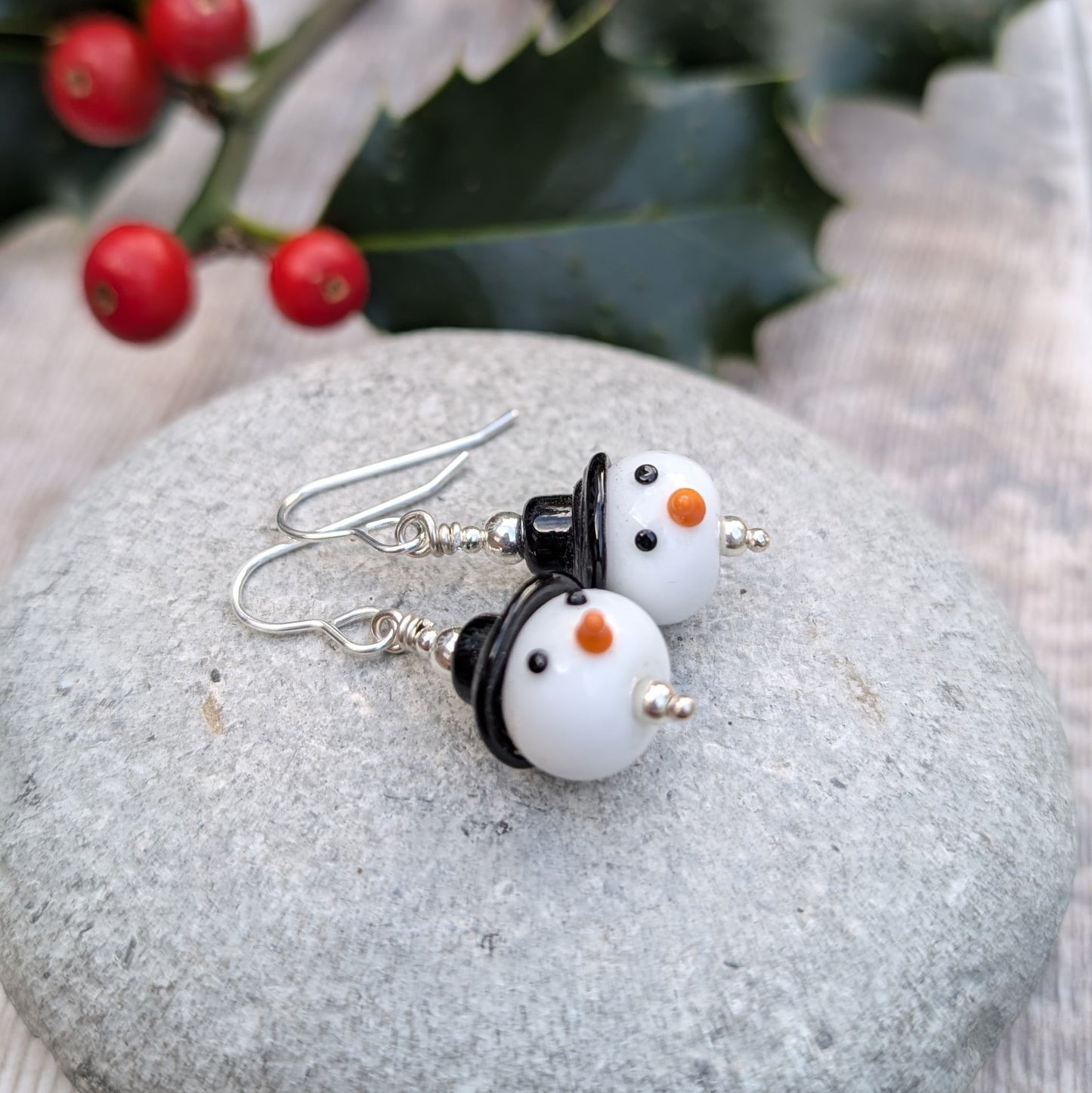 Close-up of the Silver Christmas Snowman Lampwork Glass Earrings on a stone surface, showing the rounded snowman beads with silver accents.