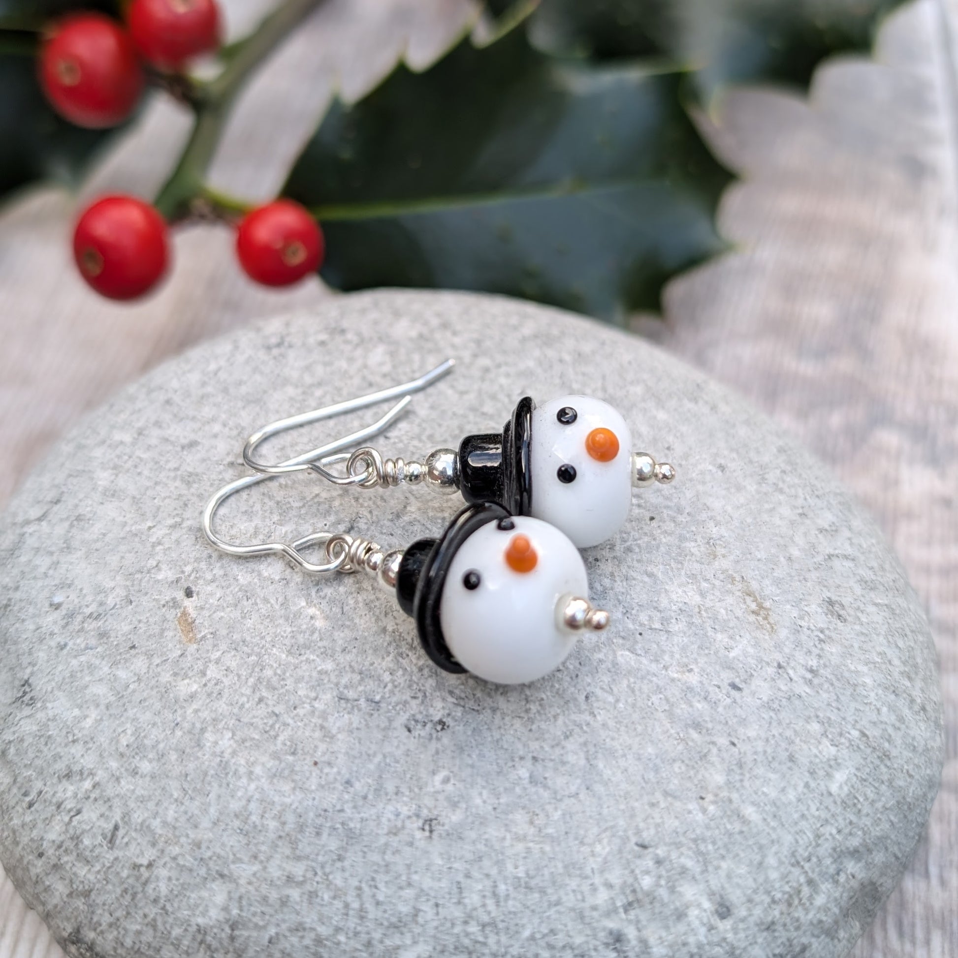 Close-up of the Silver Christmas Snowman Lampwork Glass Earrings on a stone surface, showing the rounded snowman beads with silver accents.