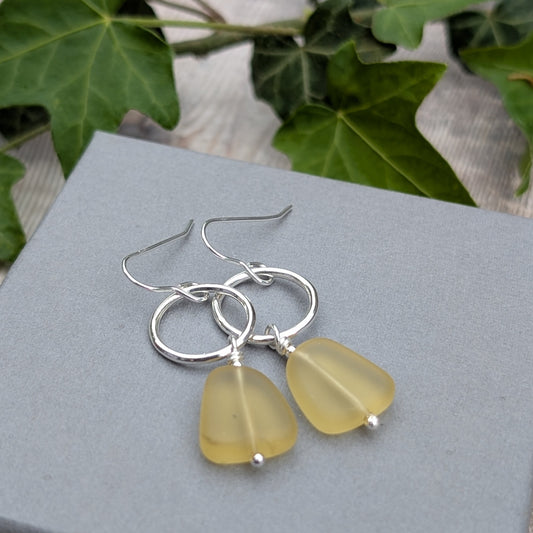 Silver Circle Earrings with Yellow Sea Glass Beads photographed on a grey jewellery box with ivy leaves behind.