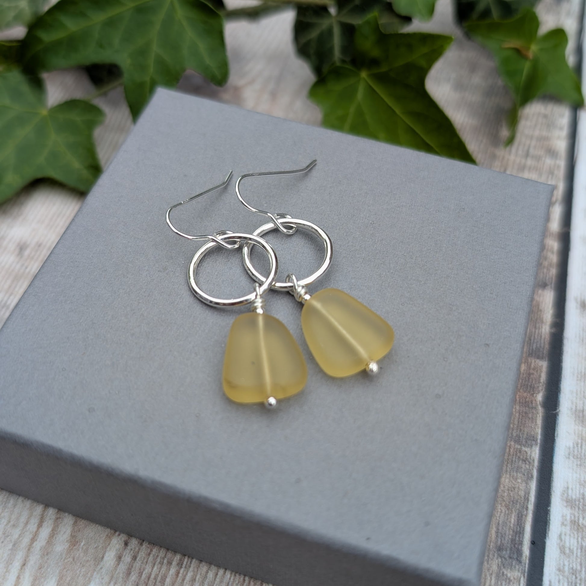 Close-up of handmade Silver Circle Earrings with Yellow Sea Glass Beads on a grey jewellery box.