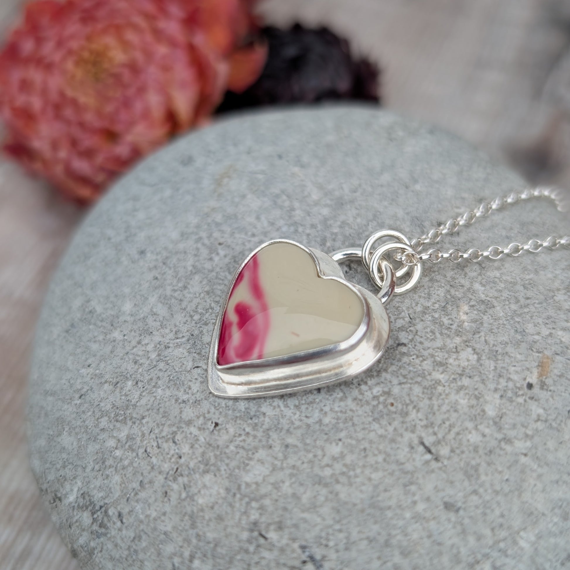 Close-up of silver heart necklace with cream and pink Surfite stone, angled view highlighting layered silver setting.