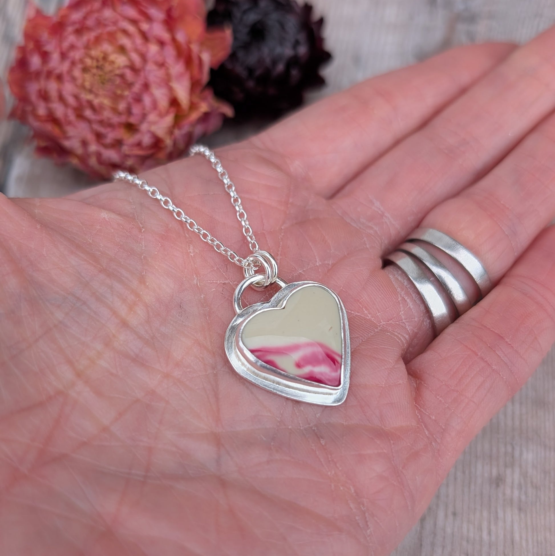Silver heart Surfite necklace resting in an open hand, showing cream and pink stone detail and scale.