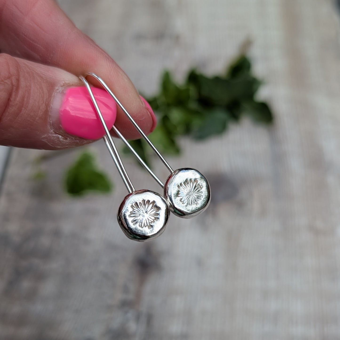 silver daisy pebble long earrings held up close, showing the polished silver pebbles and hand stamped daisy design.