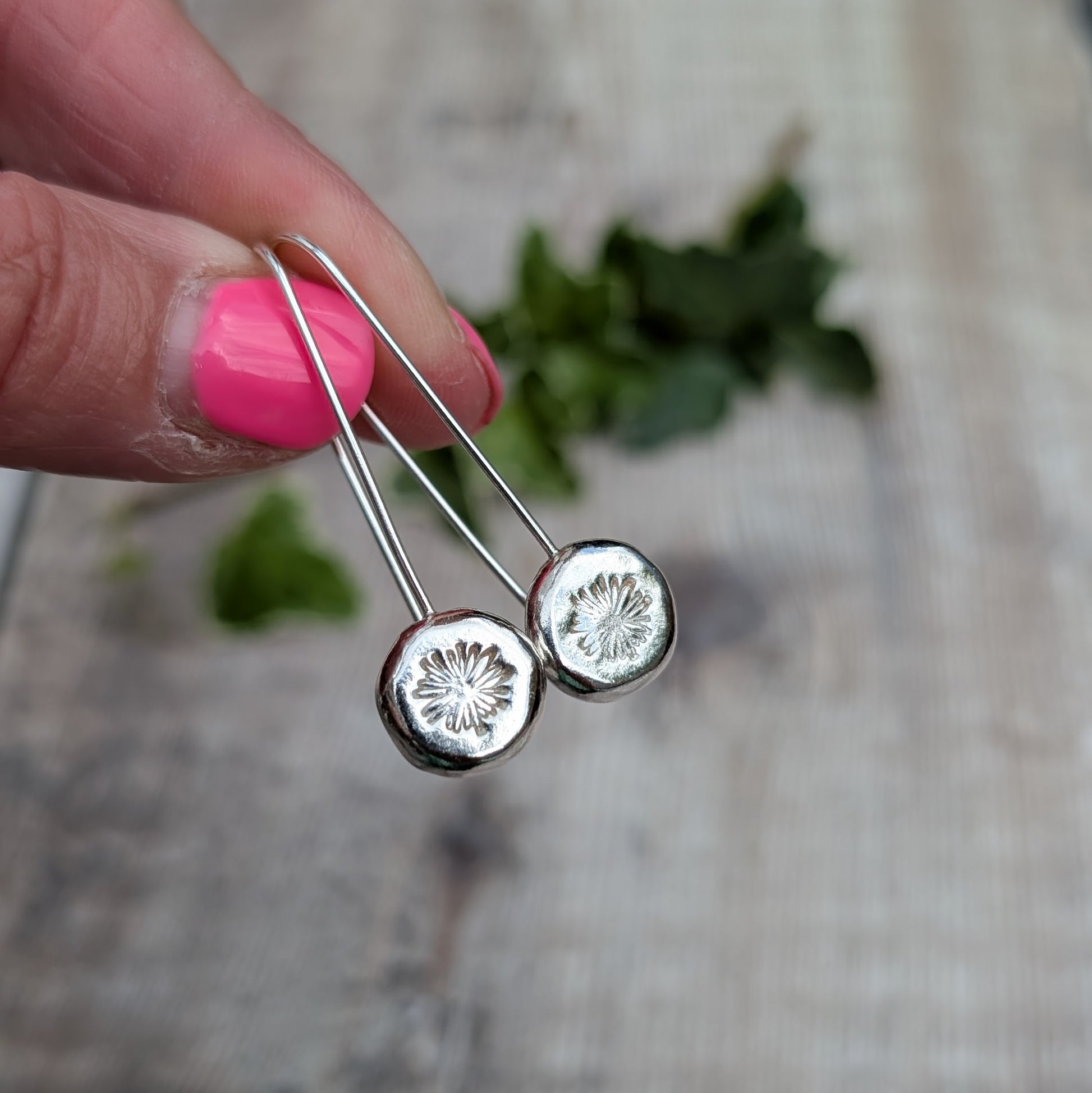 silver daisy pebble long earrings held up close, showing the polished silver pebbles and hand stamped daisy design.