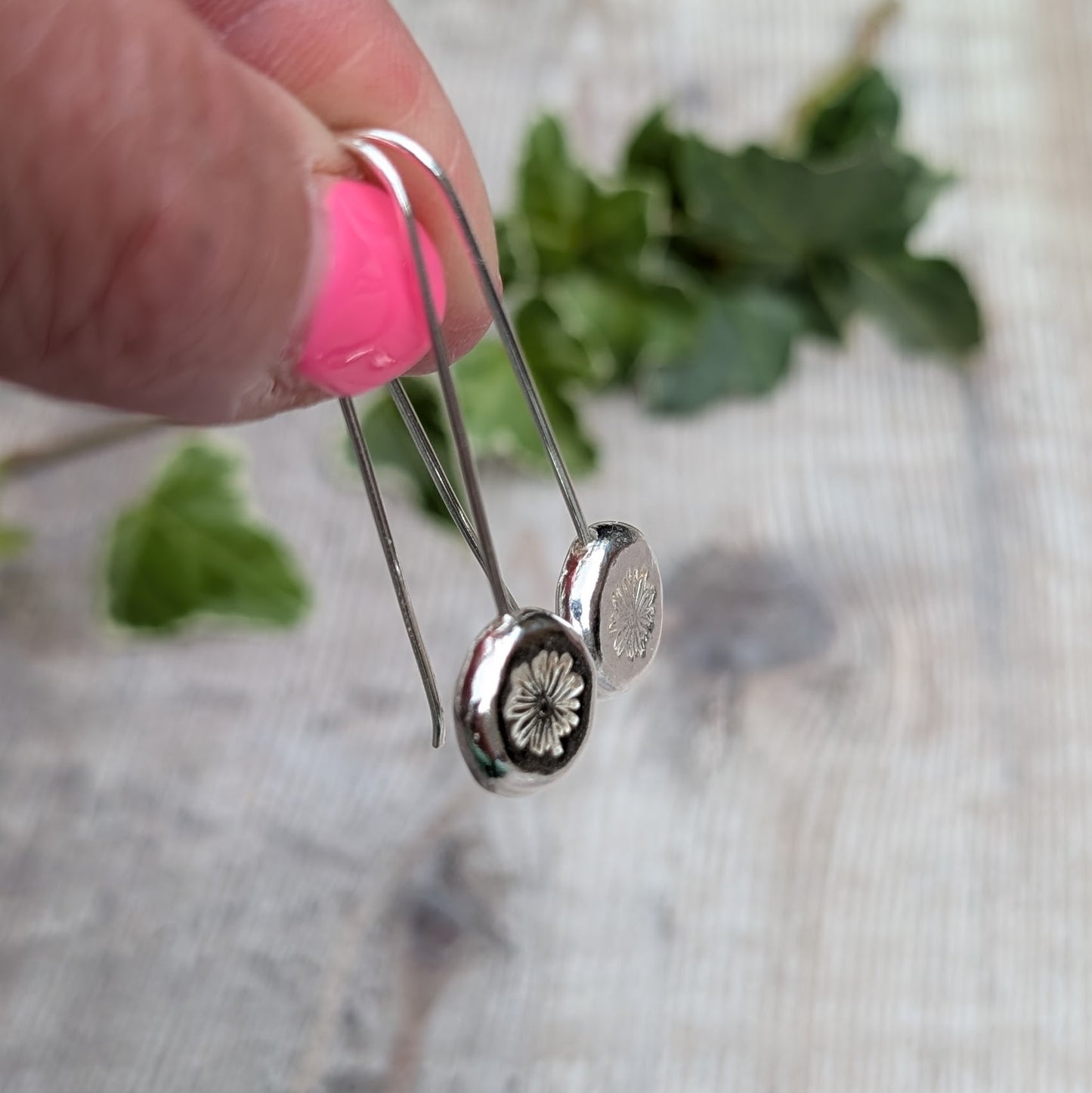 silver daisy pebble long earrings held between fingers, showing the handmade recycled Sterling Silver pebbles and stamped daisy detail.