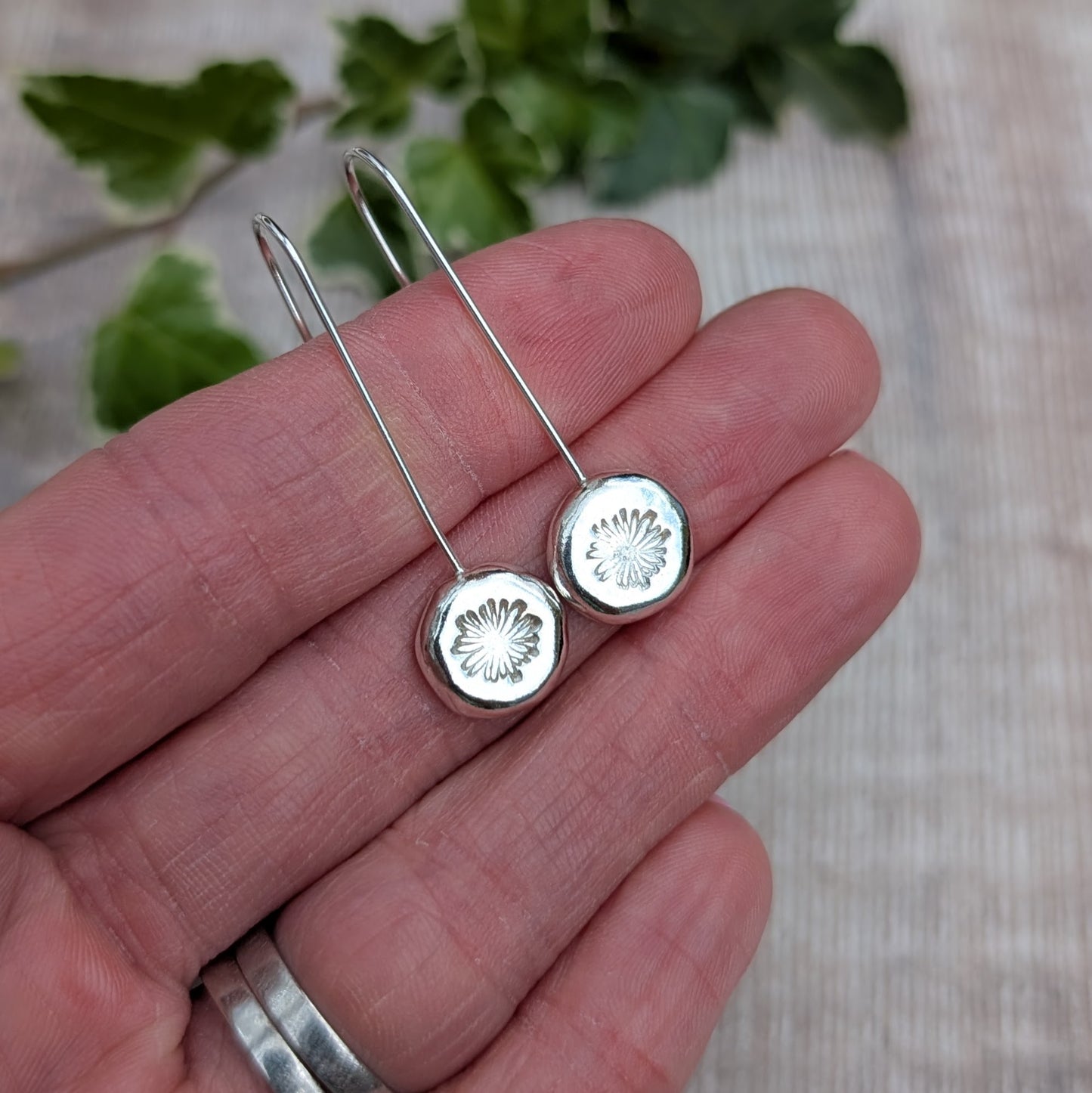 silver daisy pebble long earrings resting on a hand, showing the long ear wires and round hand stamped silver pebbles.