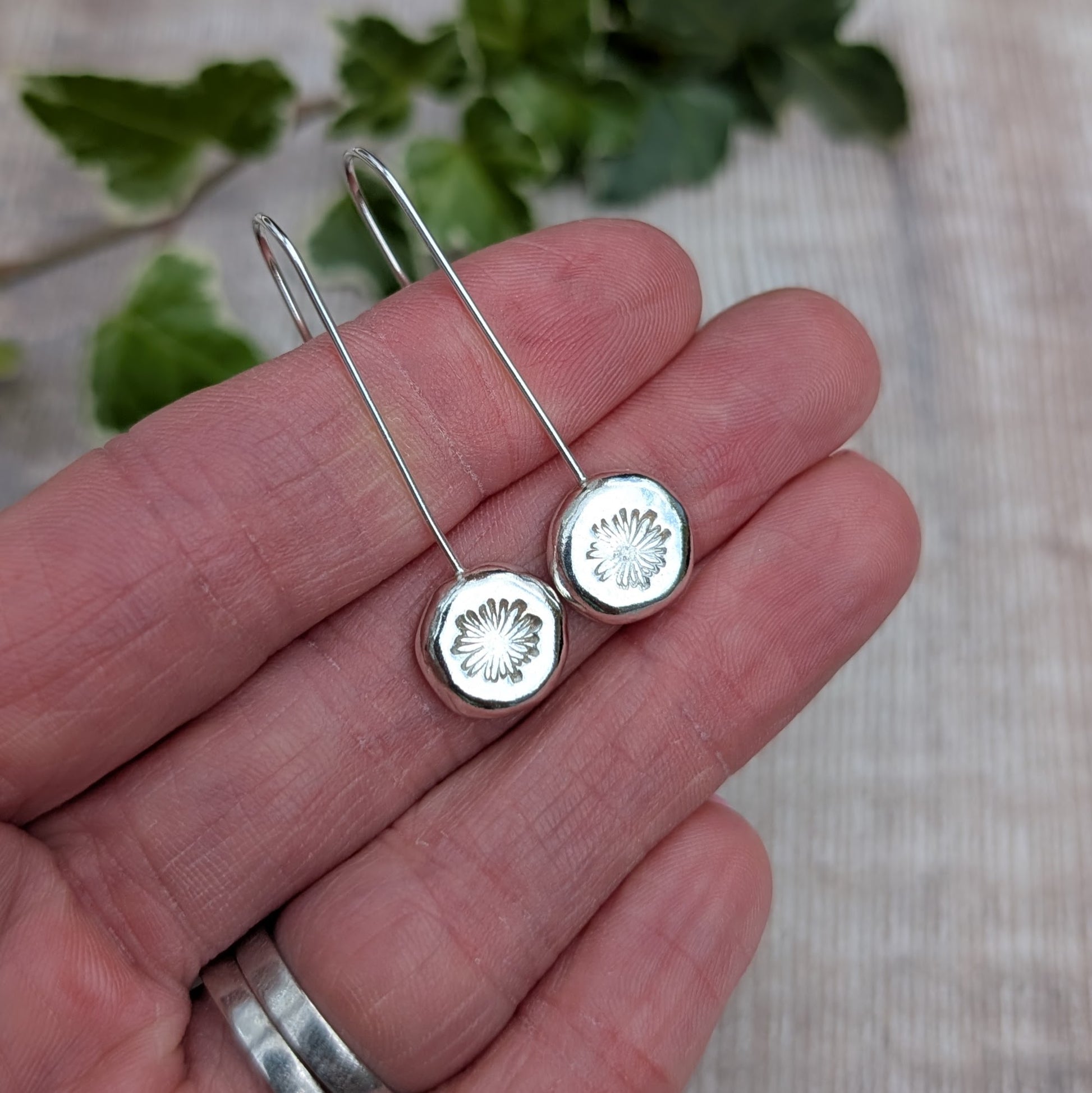 silver daisy pebble long earrings resting on a hand, showing the long ear wires and round hand stamped silver pebbles.