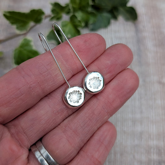 silver daisy pebble long earrings resting on a hand, showing the long ear wires and round hand stamped silver pebbles.