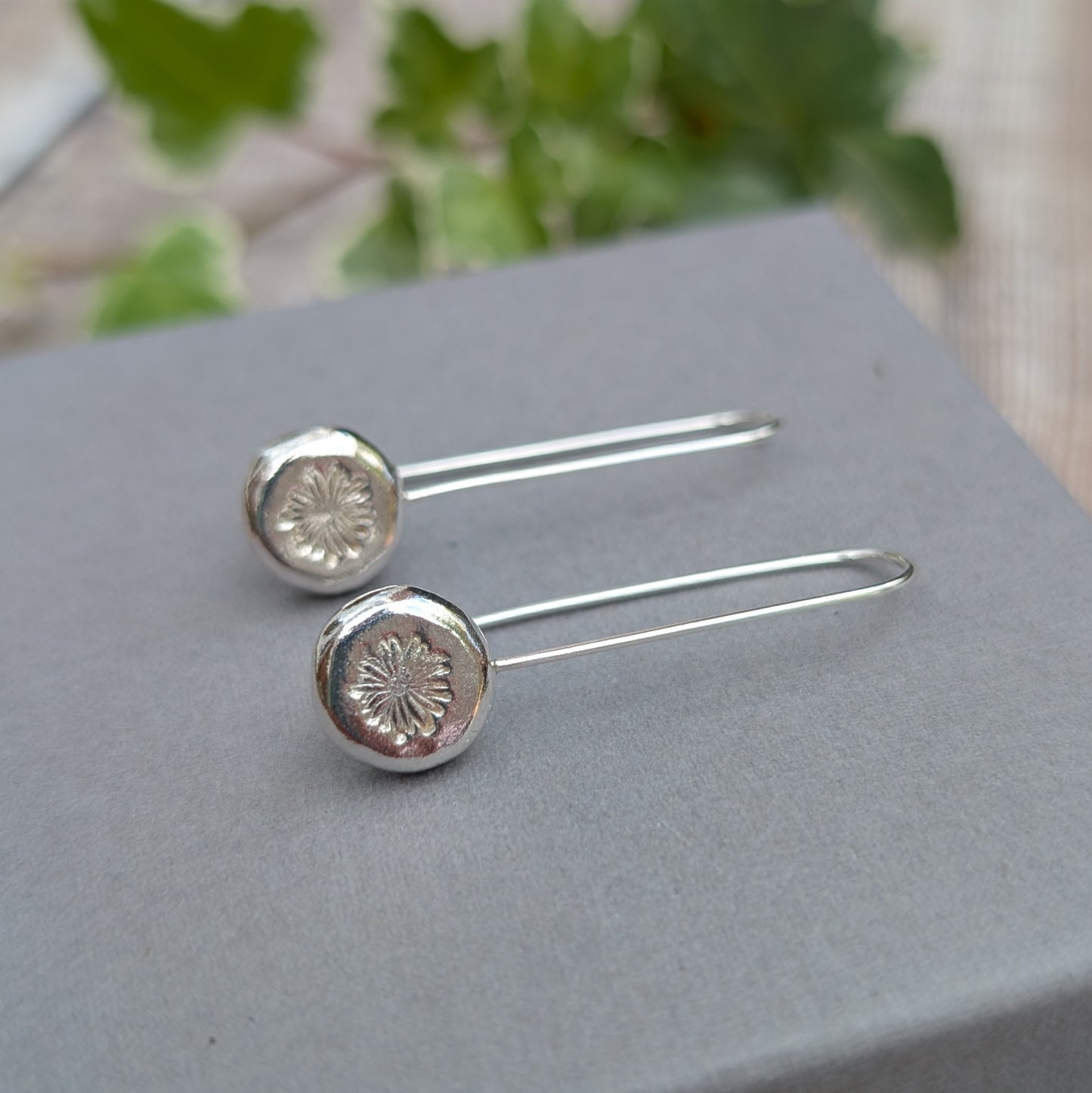 silver daisy pebble long earrings displayed on a grey jewellery box, showing the long handmade ear wires and daisy stamped pebbles.