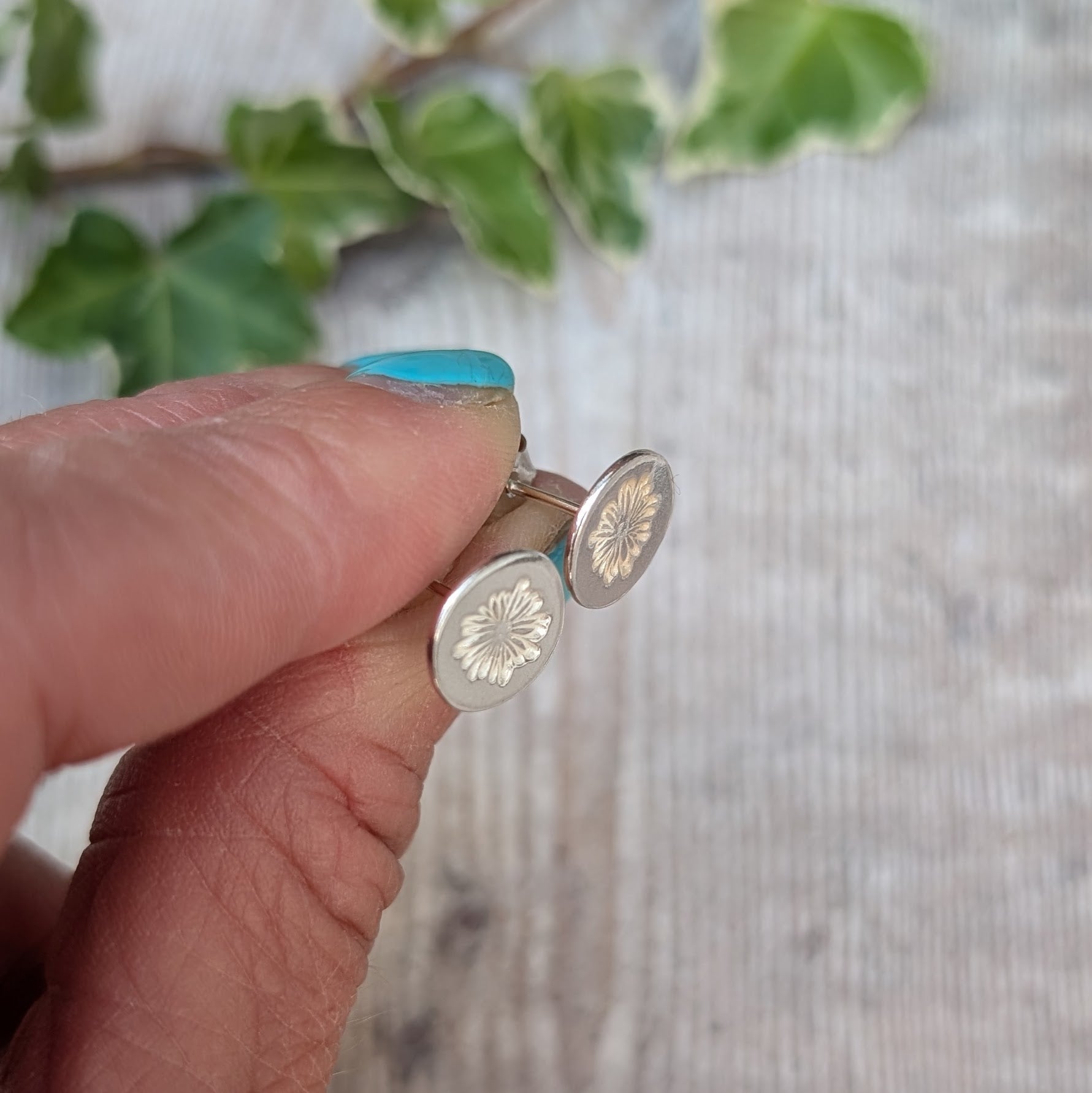 silver daisy stud earrings handmade from recycled Sterling Silver, held between fingers showing the daisy stamped design and stud posts.